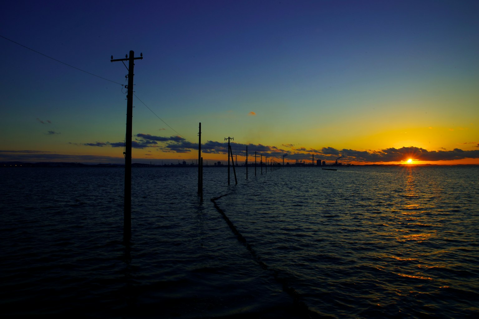 Silhouette of utility poles against a sunset over the water