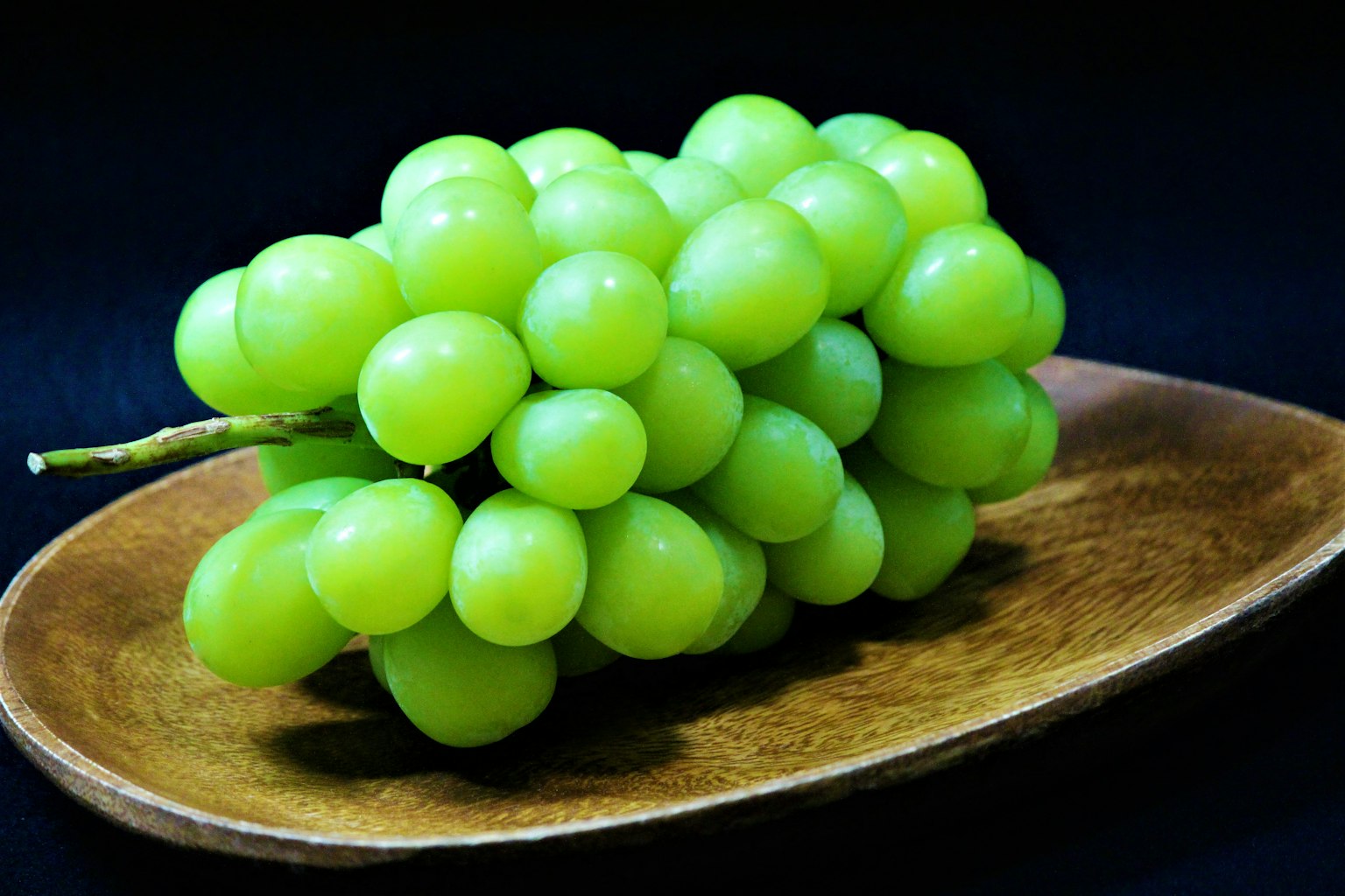 A cluster of green grapes on a wooden plate