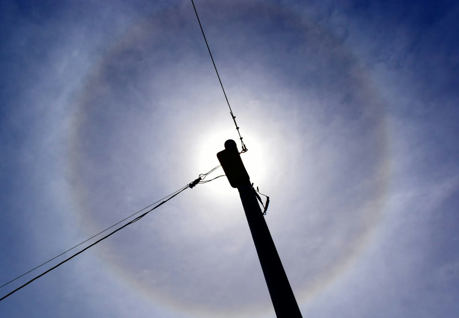 Cahaya di sekitar matahari dengan tiang listrik yang disilhouetkan di latar belakang langit biru