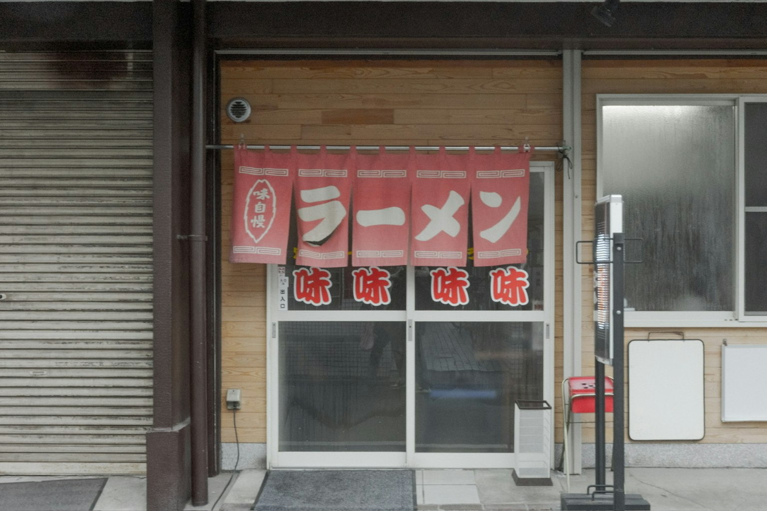 Esterno di un ristorante di ramen giapponese con tende rosse che mostrano caratteri di ramen