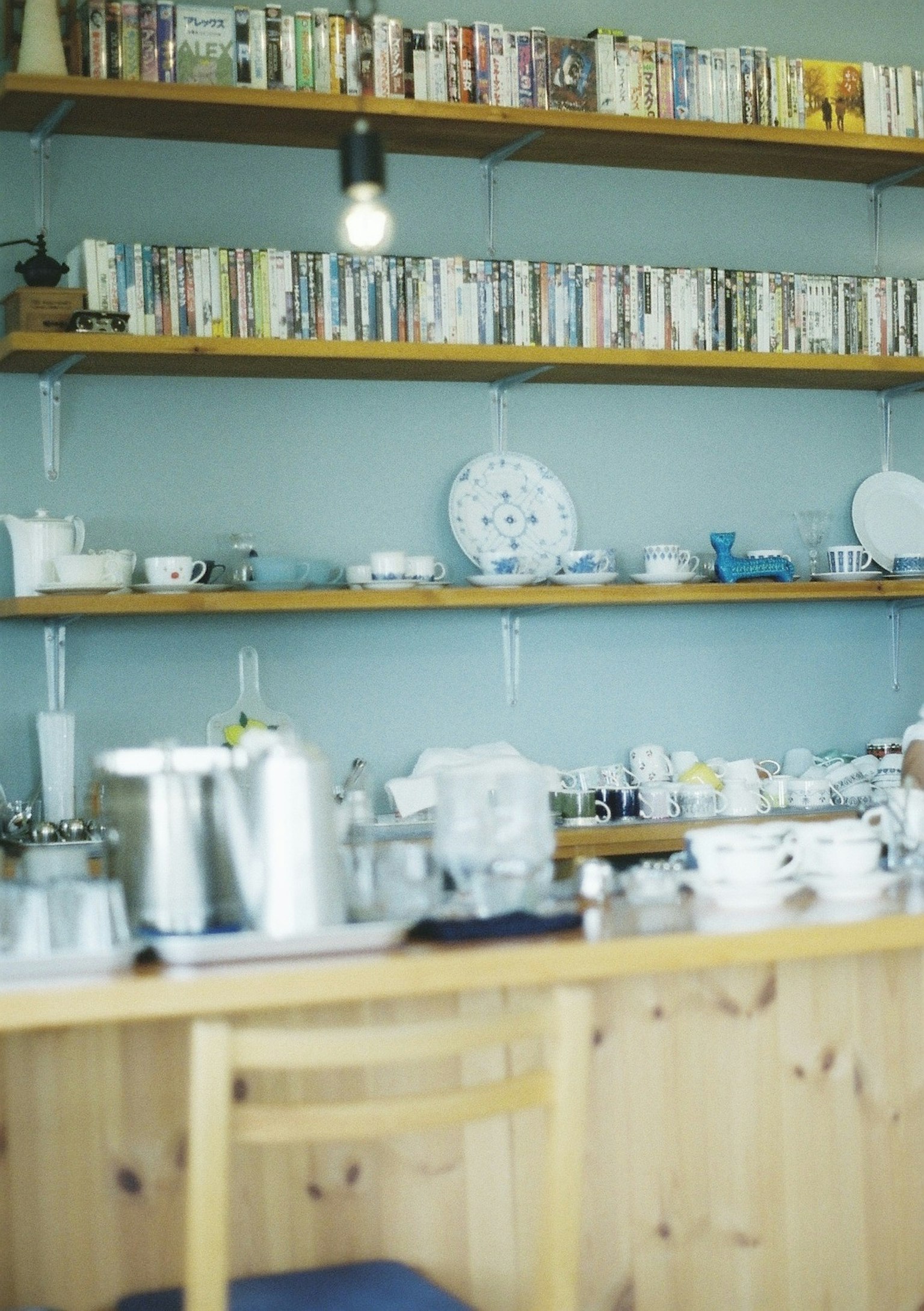 ภายในร้านกาแฟที่มีเคาน์เตอร์ไม้และชั้นวางที่เต็มไปด้วยจานและหนังสือ