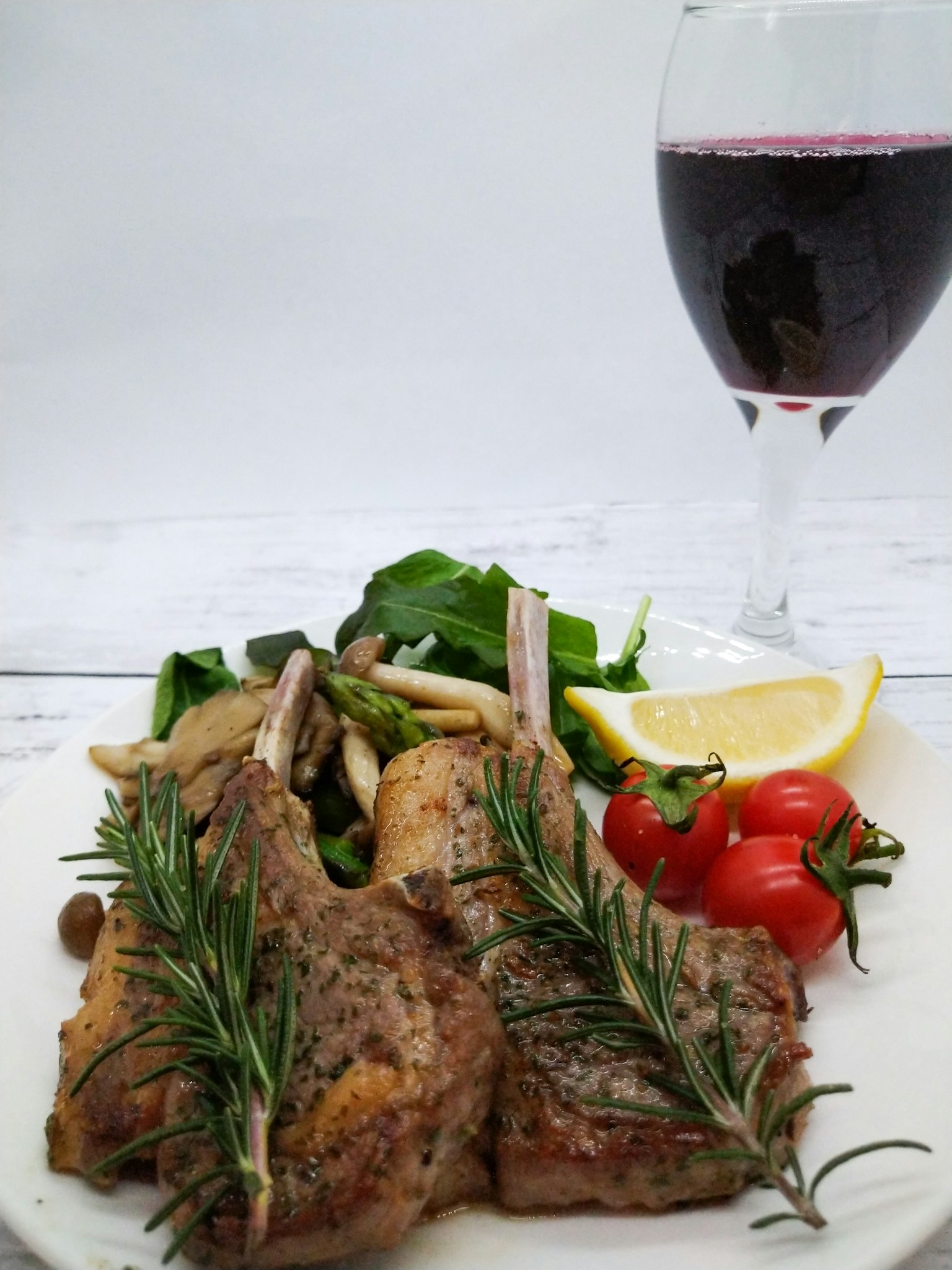 Leckere Lammkoteletts mit Salat und Cherrytomaten begleitet von Rotwein