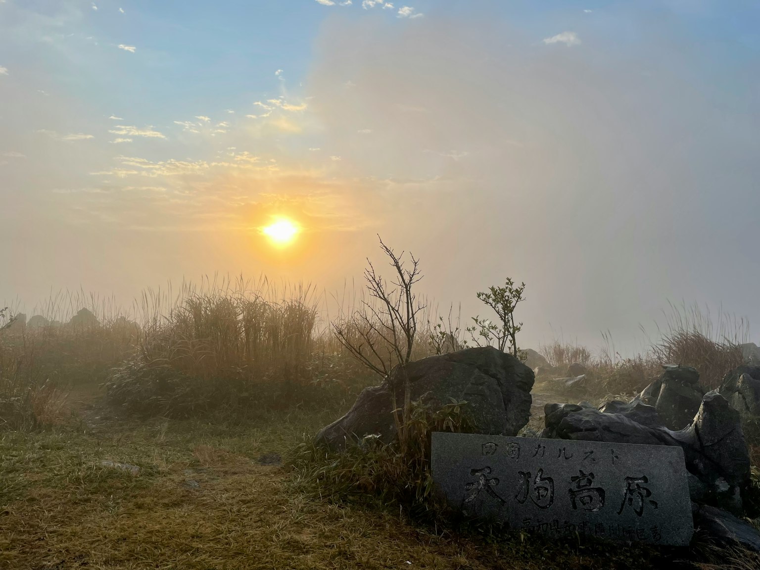 Matahari terbit melalui kabut dengan batu-batu di latar depan