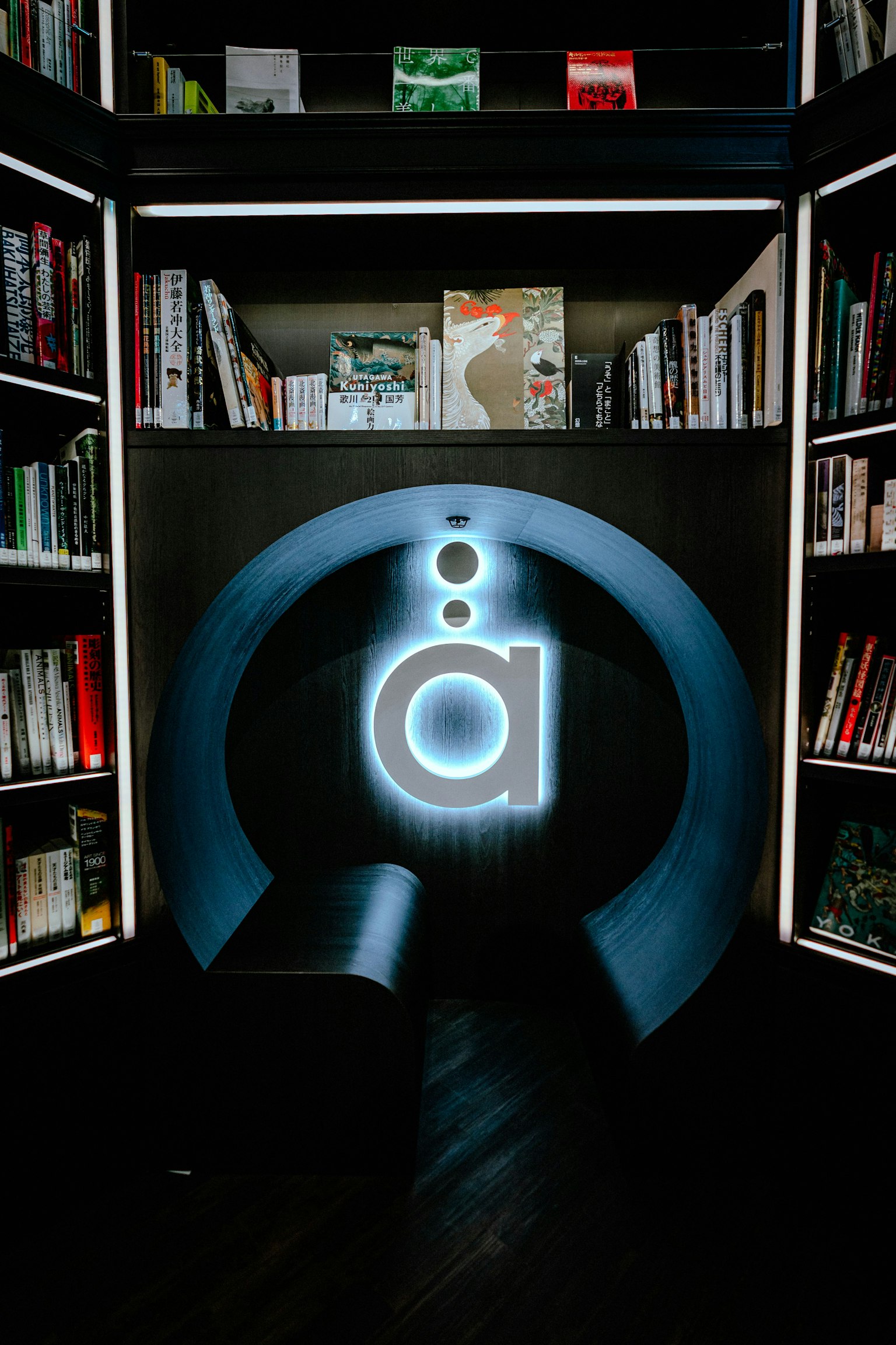 Innenansicht einer modernen Bibliothek mit Bücherregalen und einem blauen Neonlogo