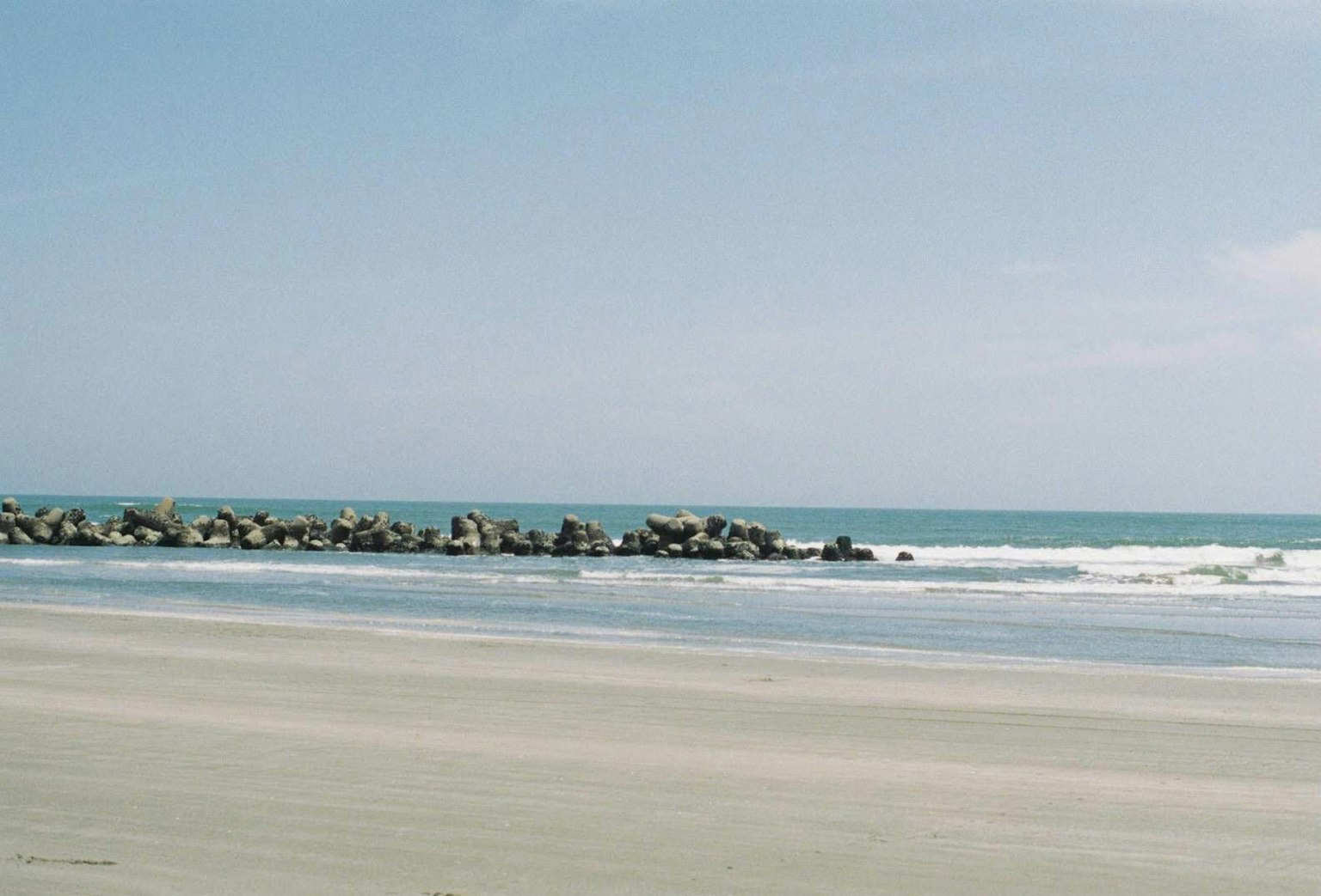 Calm sea and sandy beach scene with visible rock jetty