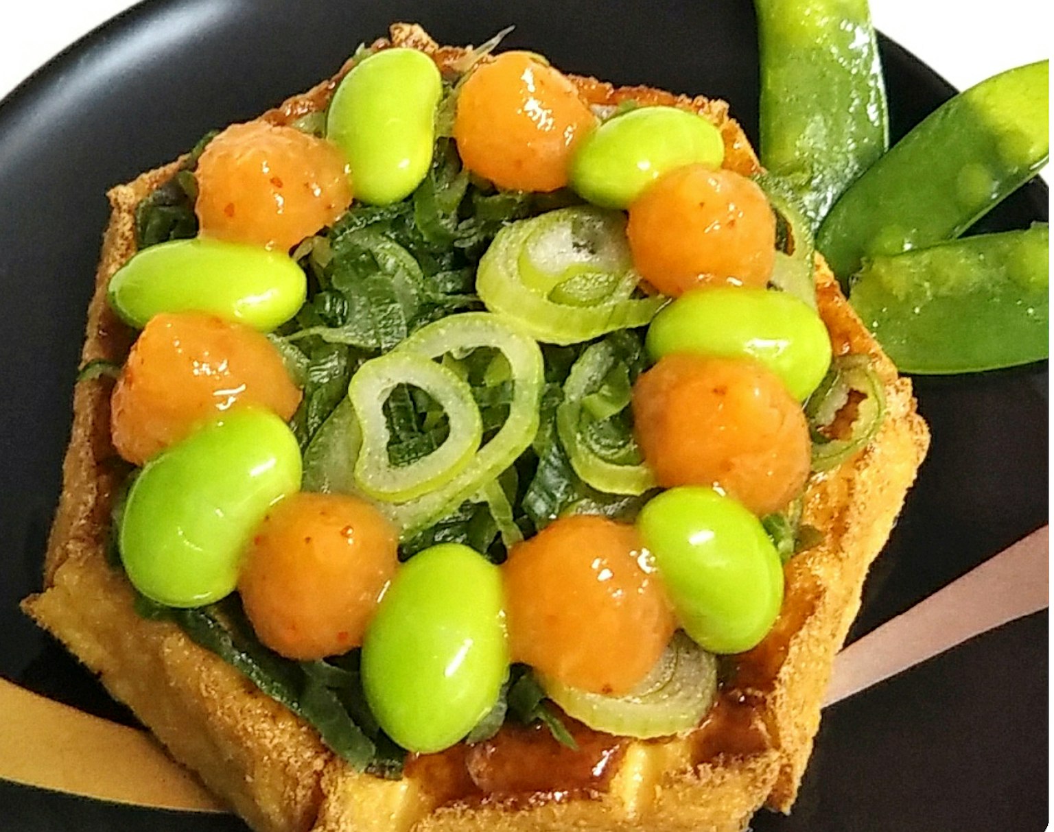 Square waffle topped with vibrant vegetables including green beans and orange melon balls
