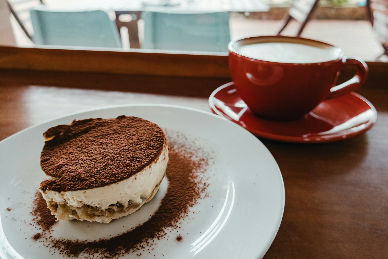 A plate of tiramisu next to a red coffee cup