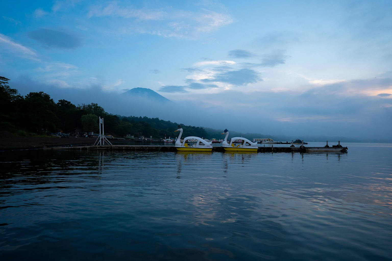 Lac serein avec des bateaux en forme de cygne jaunes et des montagnes brumeuses en arrière-plan