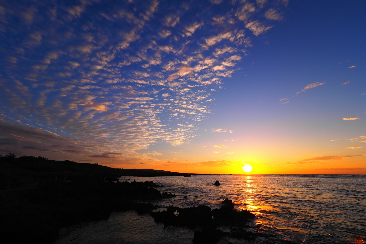 Hermoso atardecer sobre el océano con colores vibrantes y patrones de nubes reflejándose en el agua