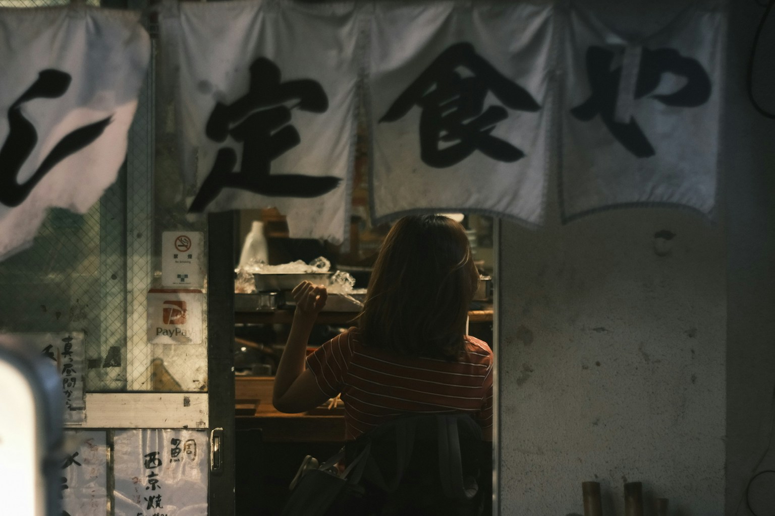 Intérieur d'une petite cantine avec une femme cuisinant et une signalisation japonaise