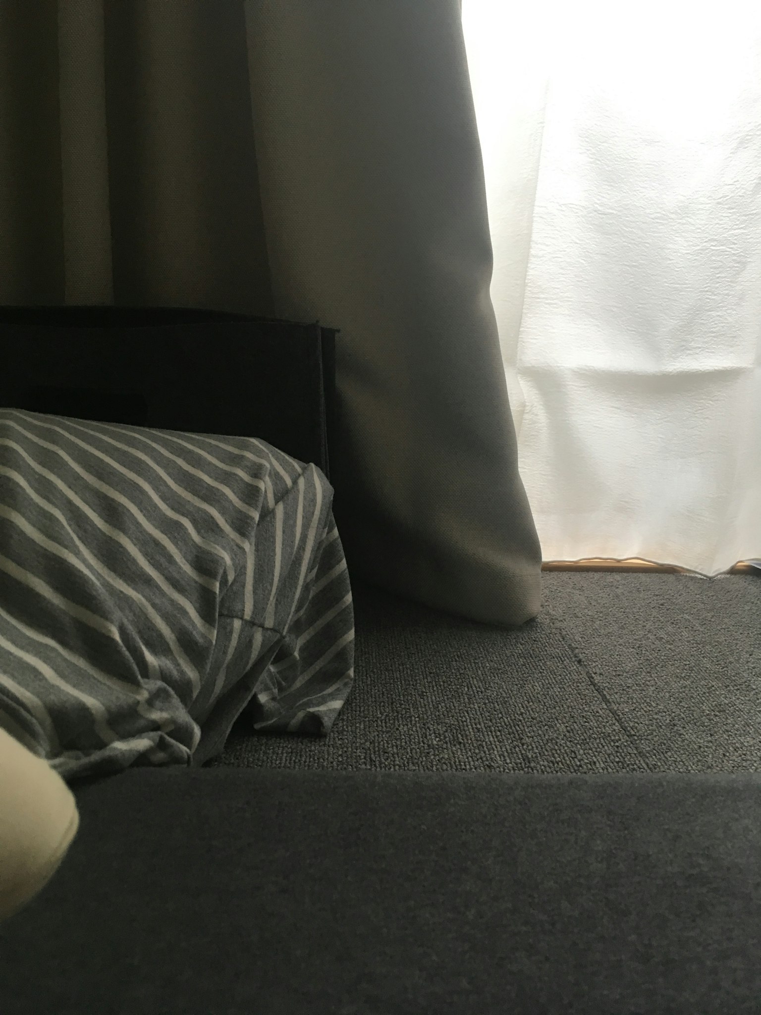 Eine einfache Ecke eines Raumes mit einem weißen Vorhang und einem gestreiften Bettbezug