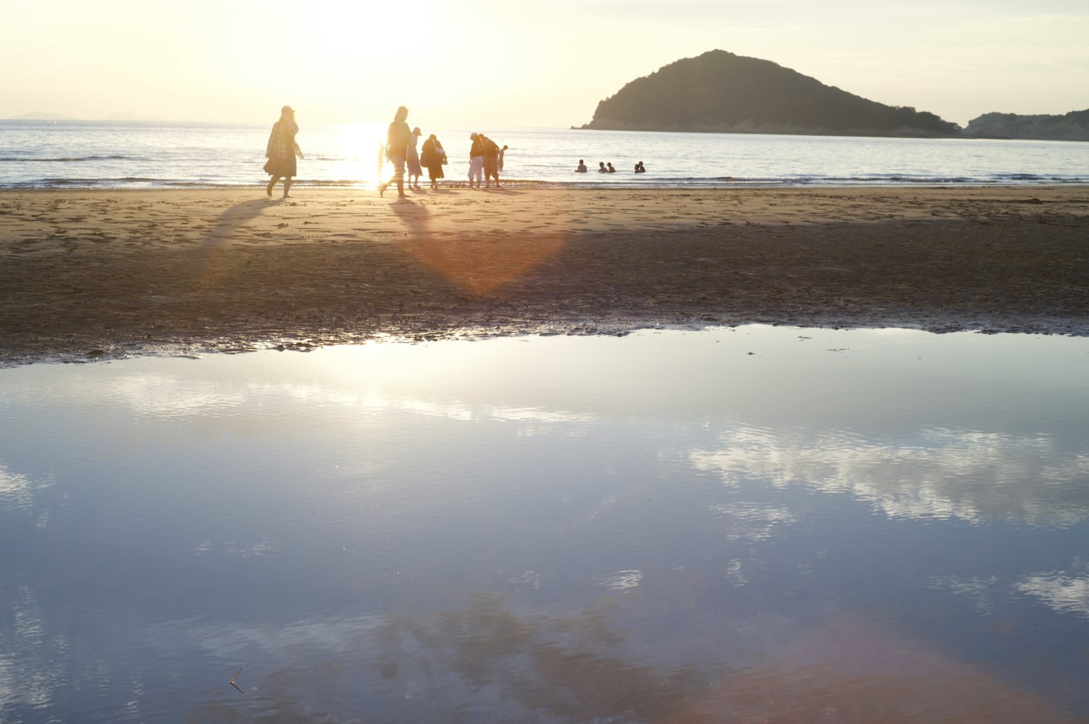 People enjoying the beach at sunset with reflections