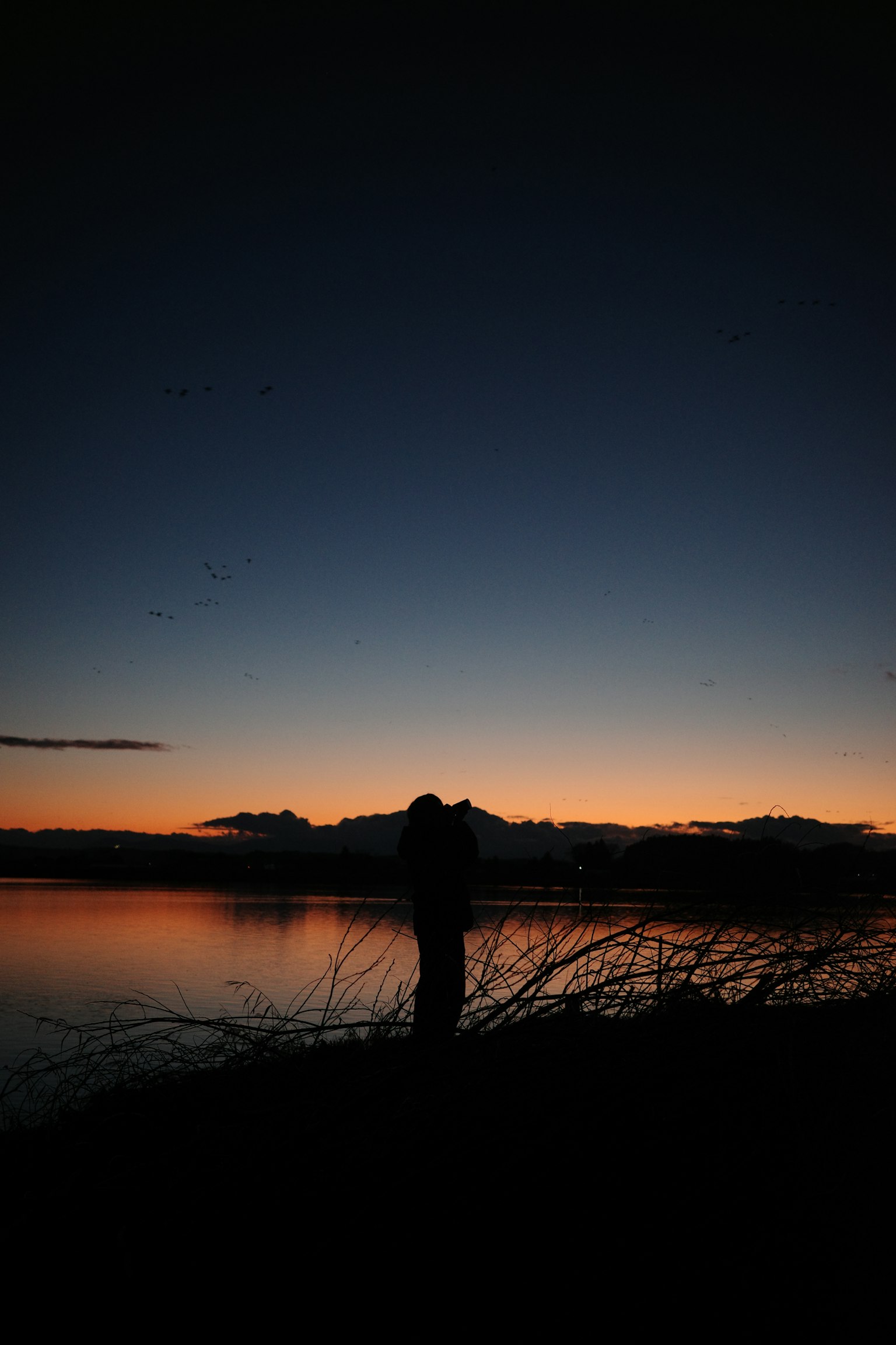 Silhouette einer Person, die am Abend an einem See steht