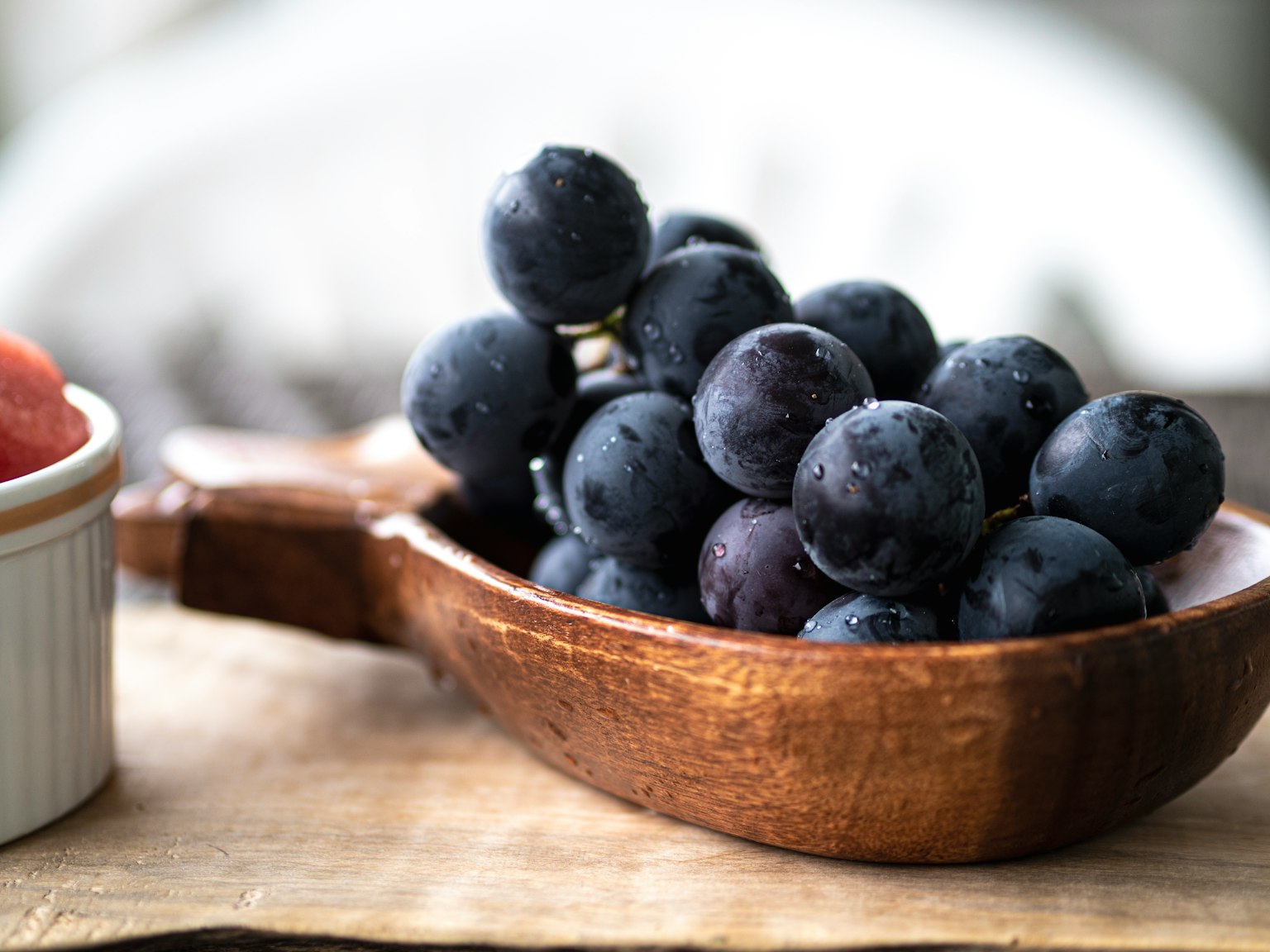 Uva fresca in un cucchiaio di legno con fragole in un piccolo piatto bianco