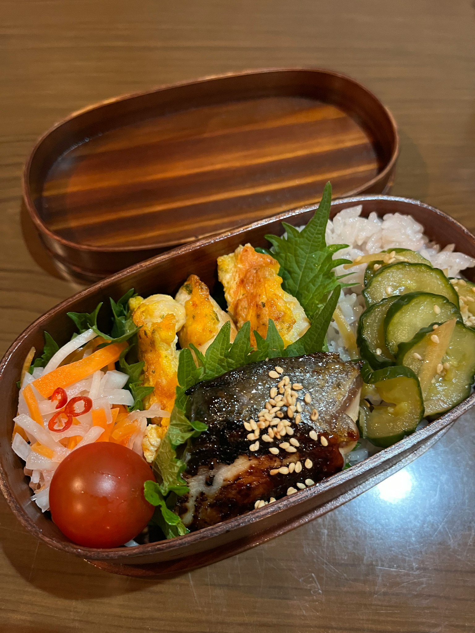 便当盒内有米饭、烤鱼、鸡蛋卷、蔬菜和番茄