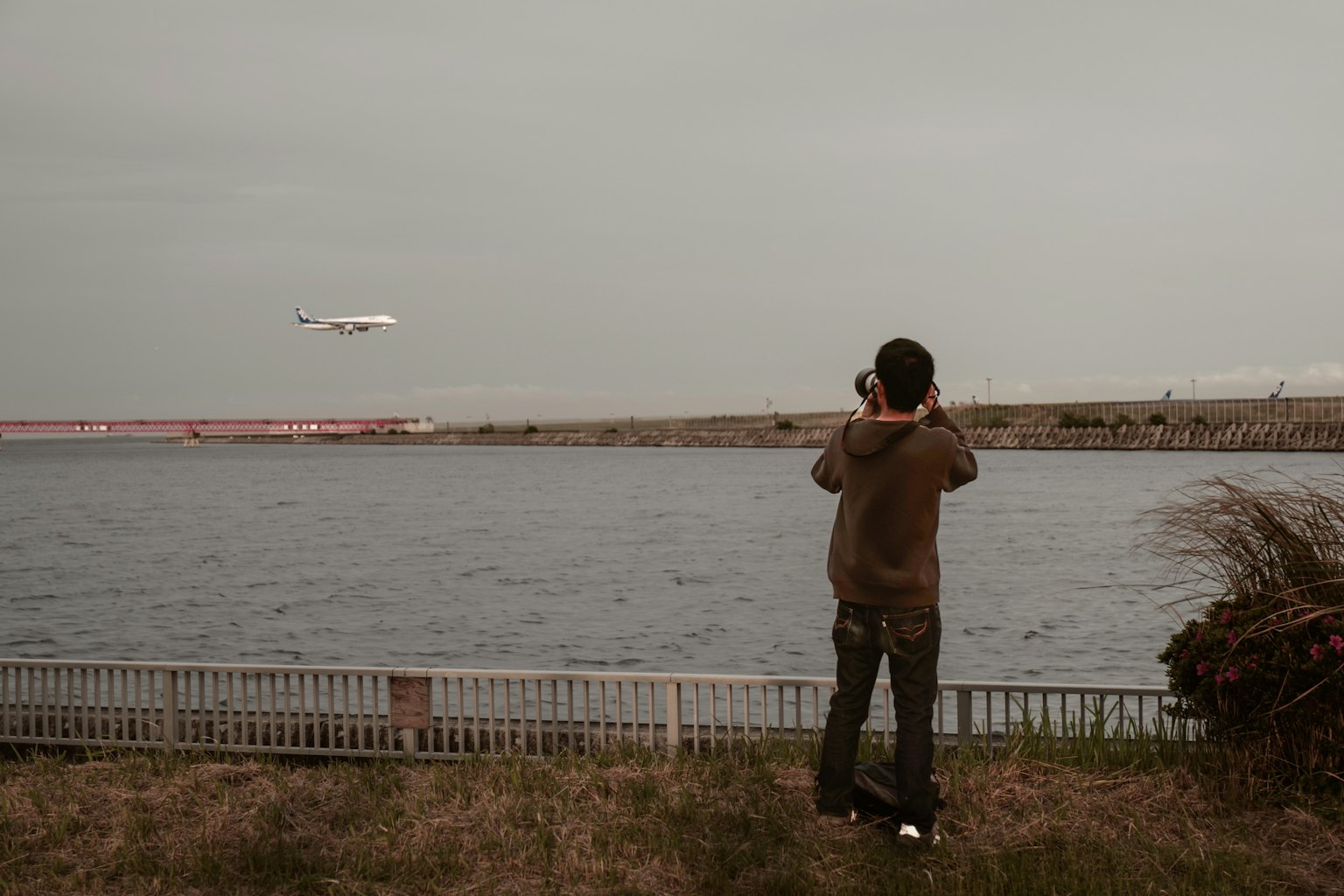 一名男子站在河边拍摄飞机