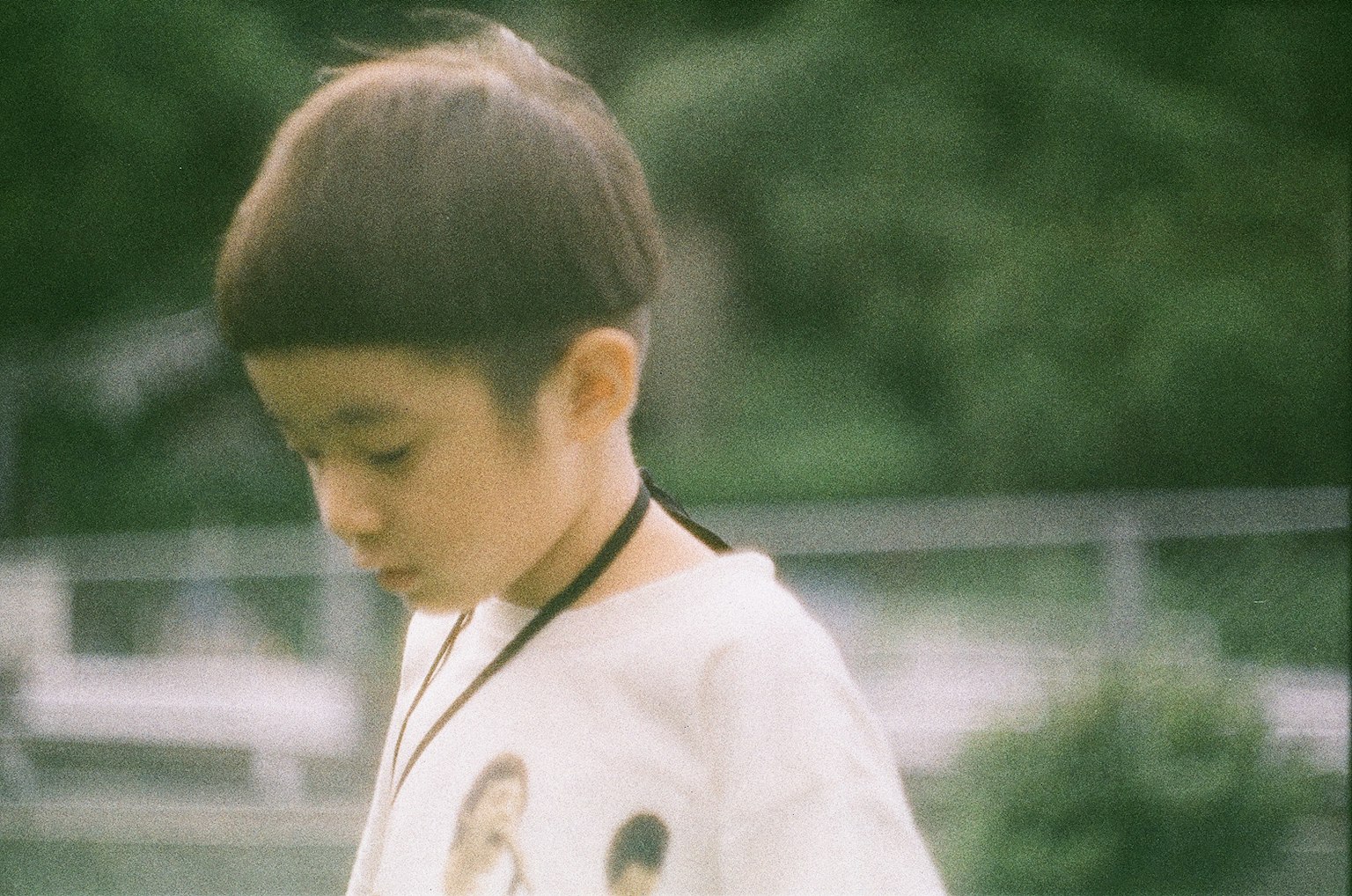 髪型が特徴的な子供が外で遊んでいる様子で、白いTシャツにプリントがある