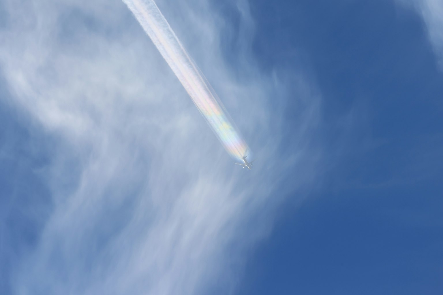Weiße Wolken und regenbogenfarbiger Kondensstreifen im blauen Himmel