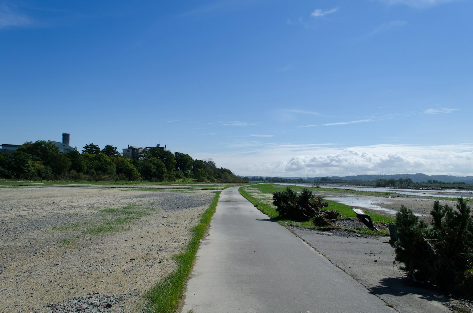 A riverside walkway under a blue sky with greenery and distant hills