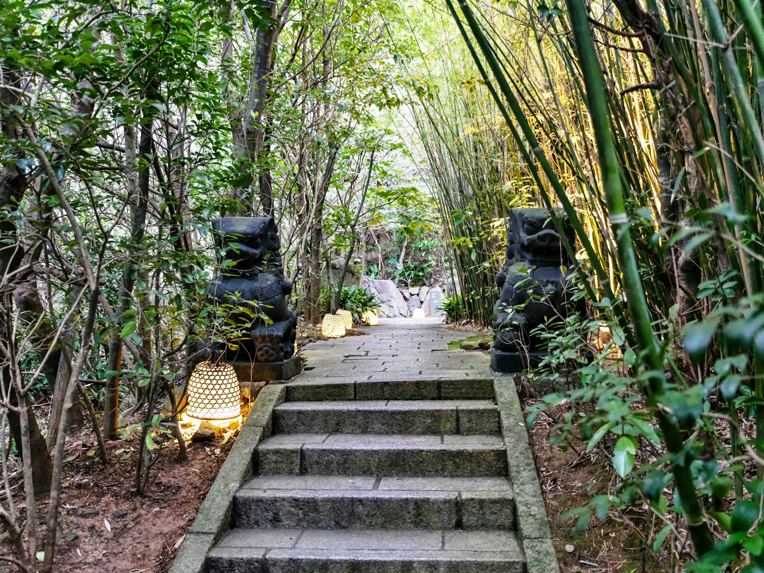 Tangga batu yang mengarah melalui hutan bambu dengan lentera