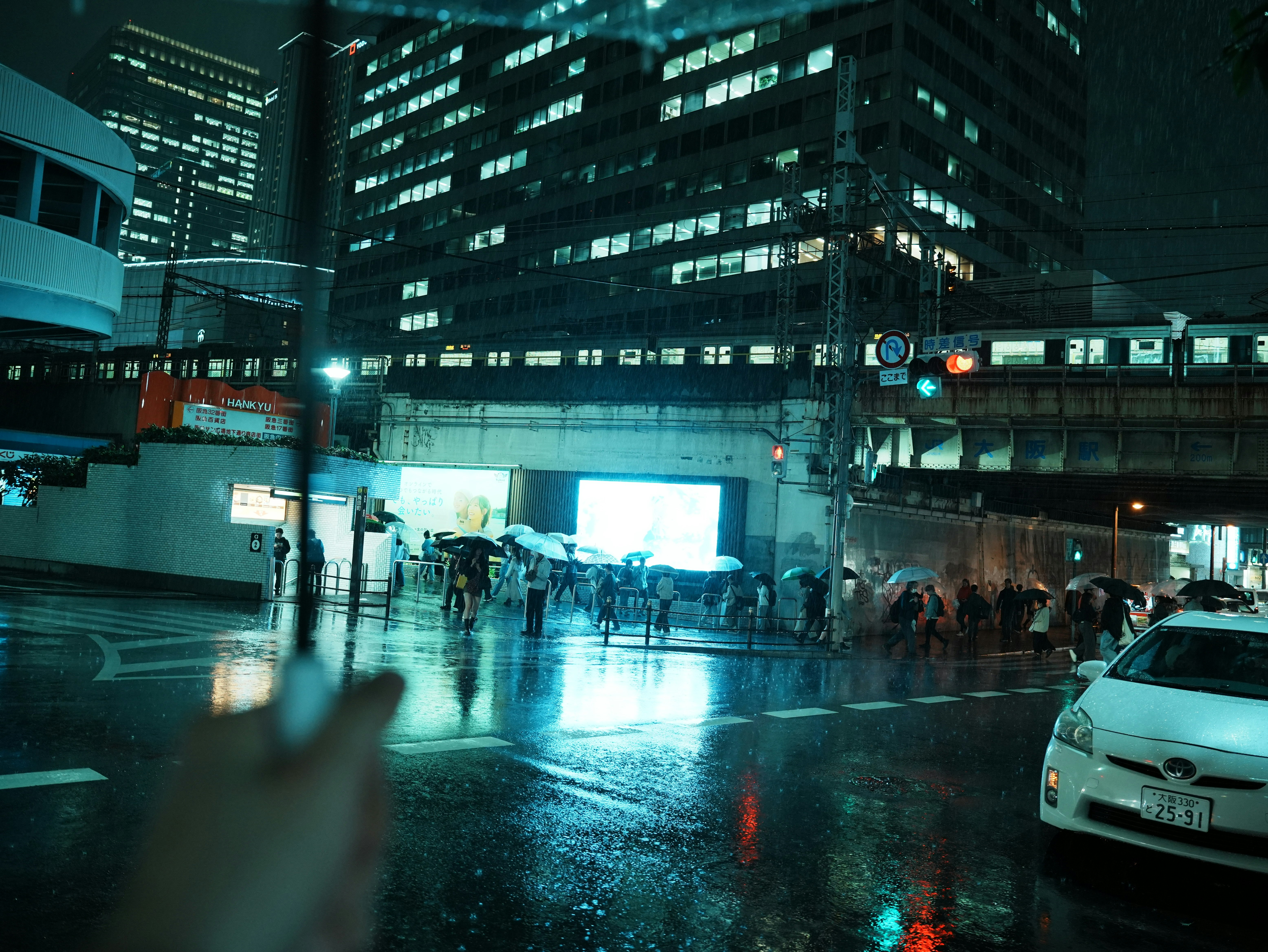 雨の大阪の夜、ビル街の濡れた路面と人々