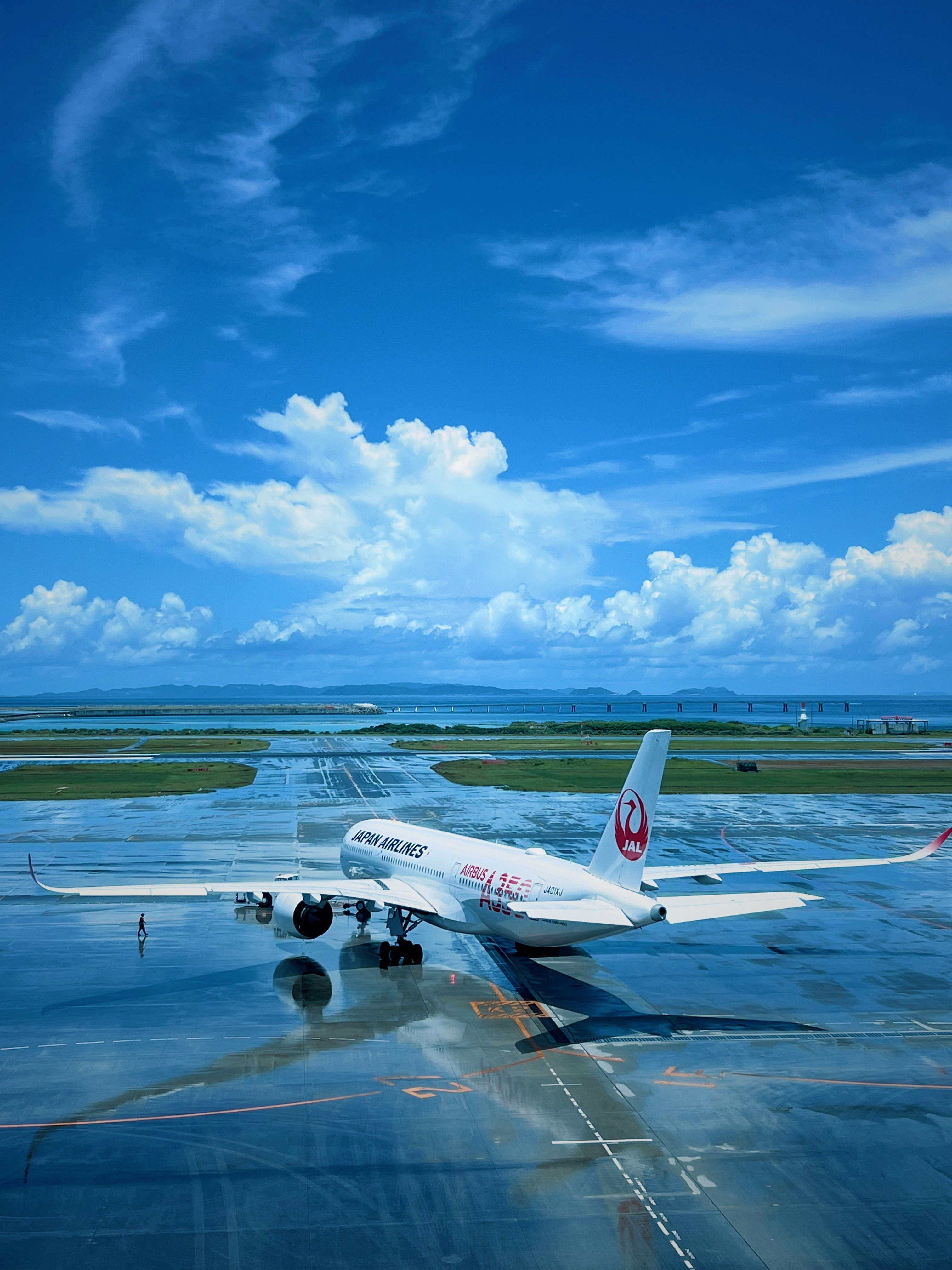 Japan Airlines aircraft taxiing on the runway at Naha Airport after the rain under a blue sky