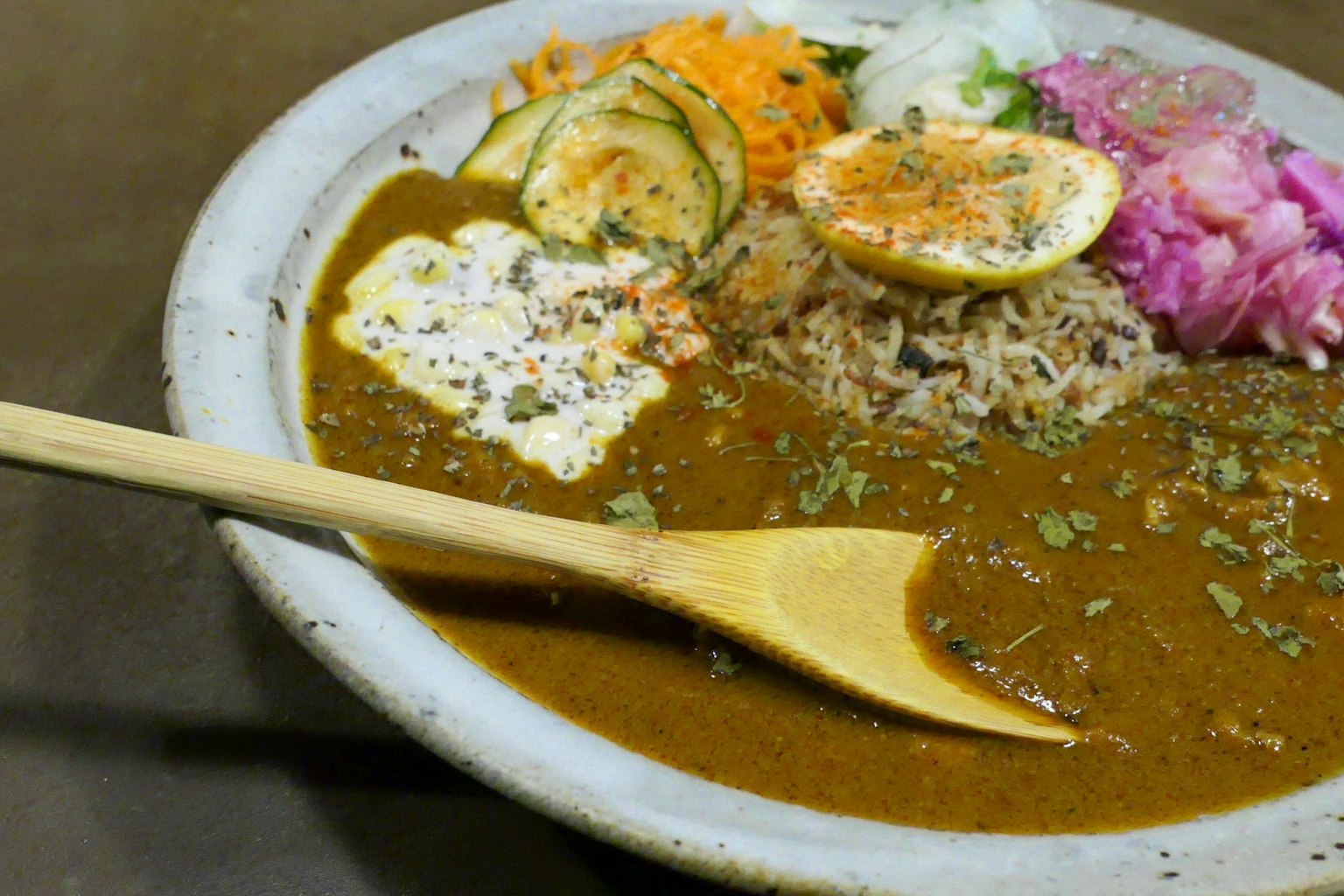 Arroz con curry servido con guarniciones de verduras frescas y una cuchara de madera