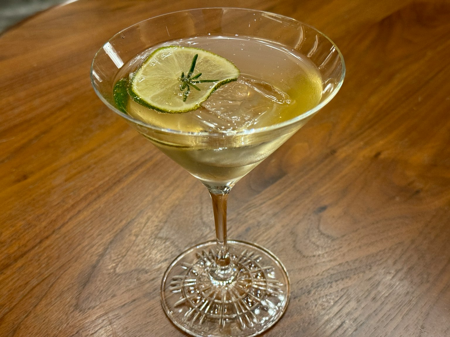 Un bicchiere da cocktail con una bevanda guarnita con una fetta di lime e erbe