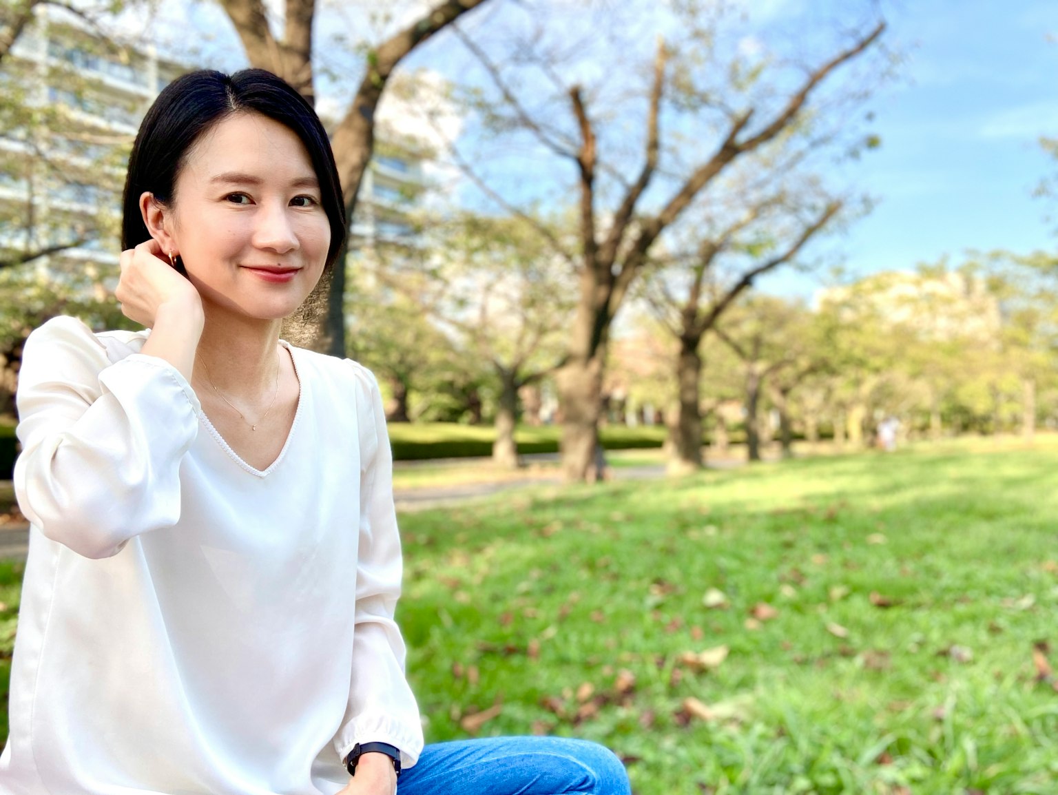 一位女性在公園微笑 背後是綠色草地和樹木