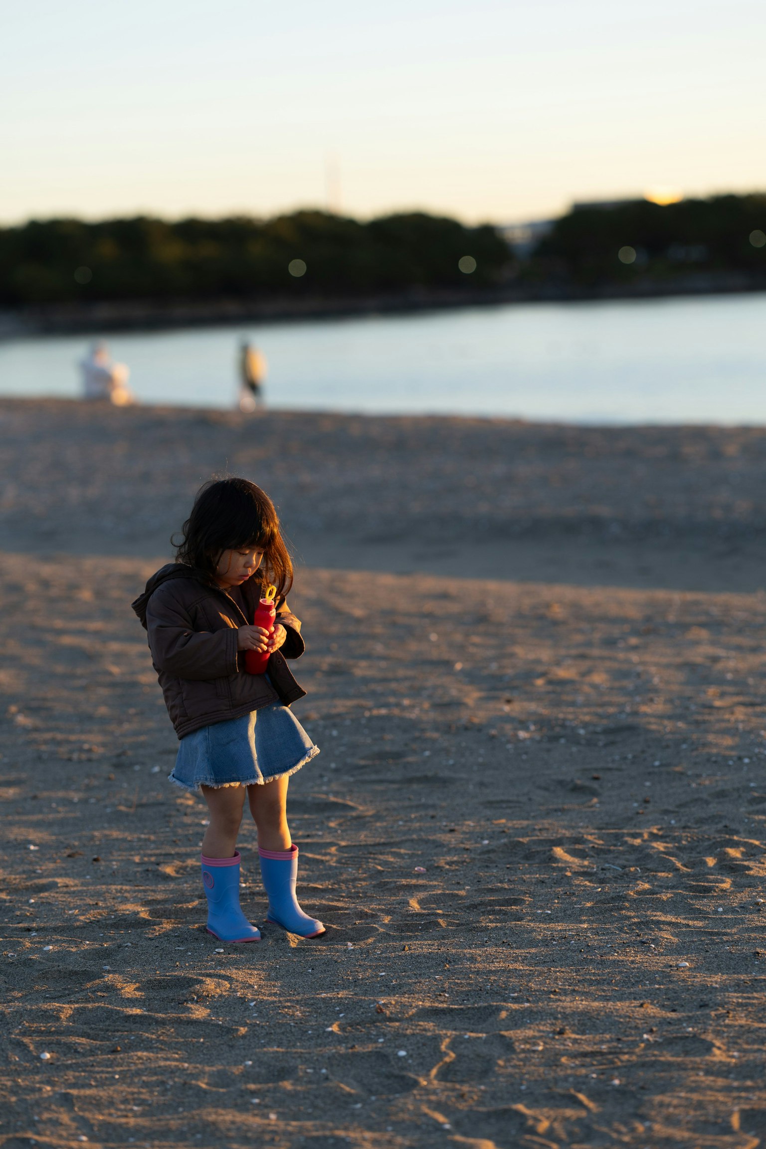 Niño jugando en la playa al atardecer con botas azules