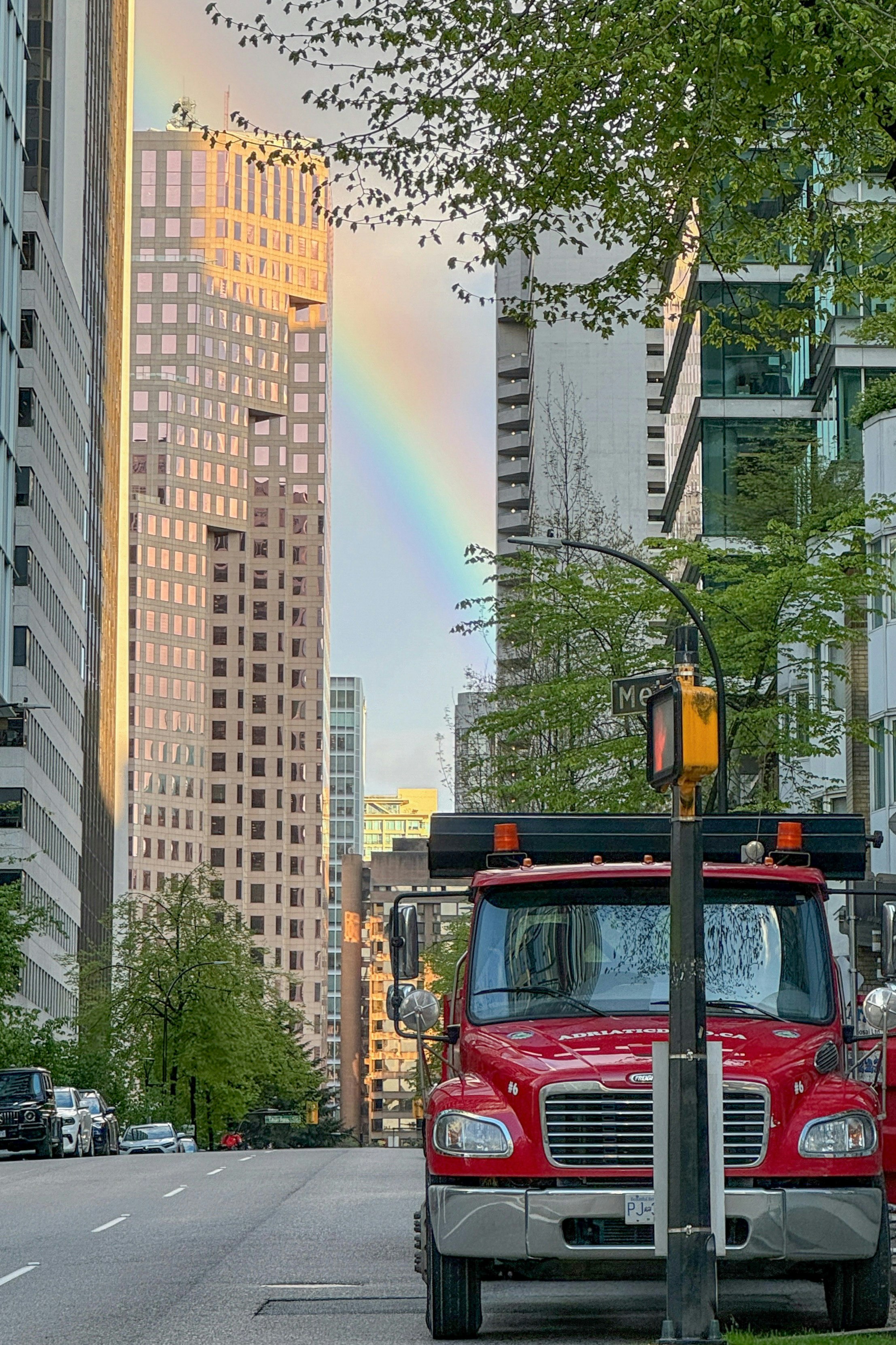 高層ビル街の道路にかかる虹と赤い車