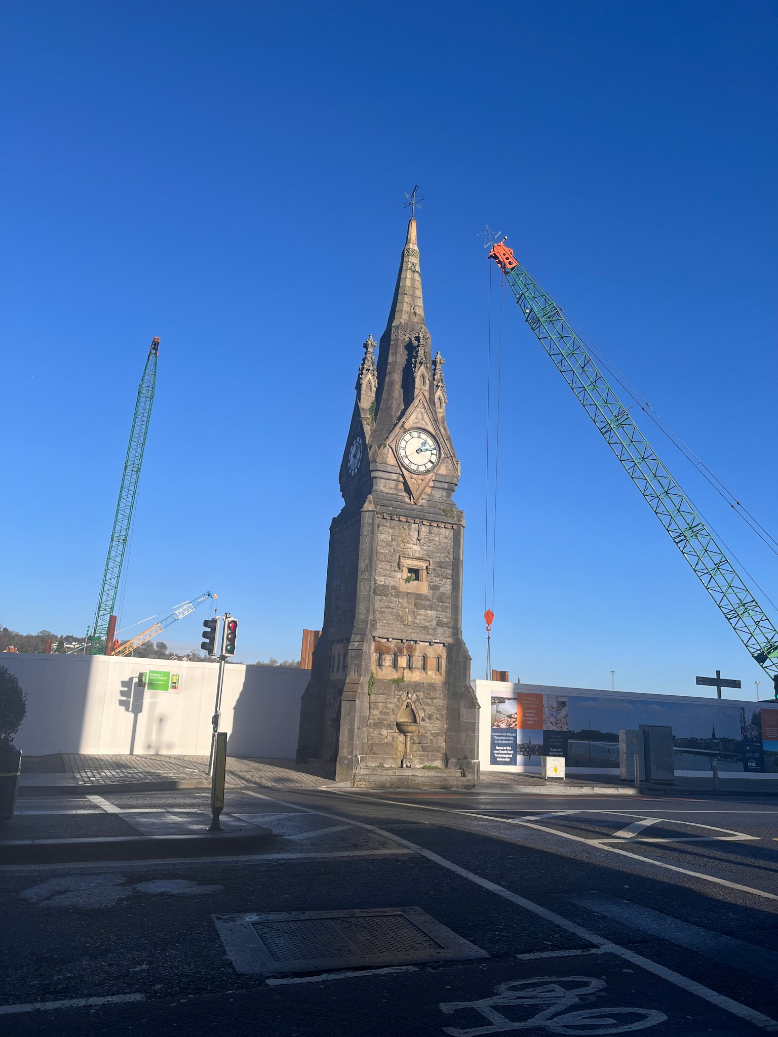 Old clock tower under a clear blue sky with construction cranes
