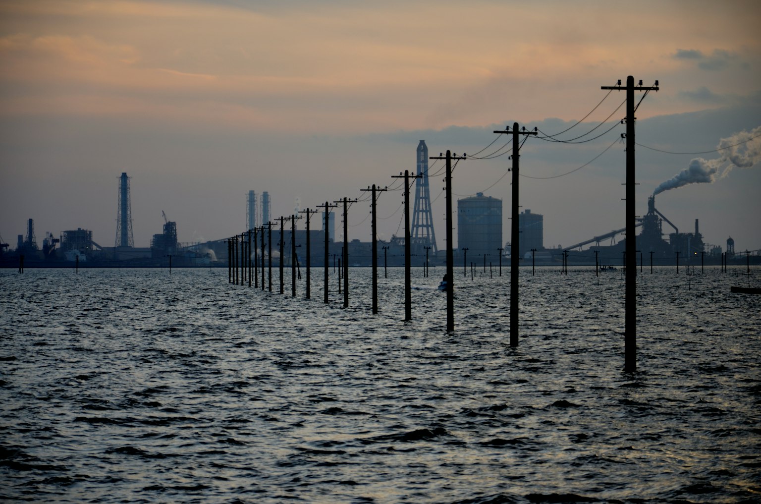 Power lines emerging from water with industrial skyline at sunset