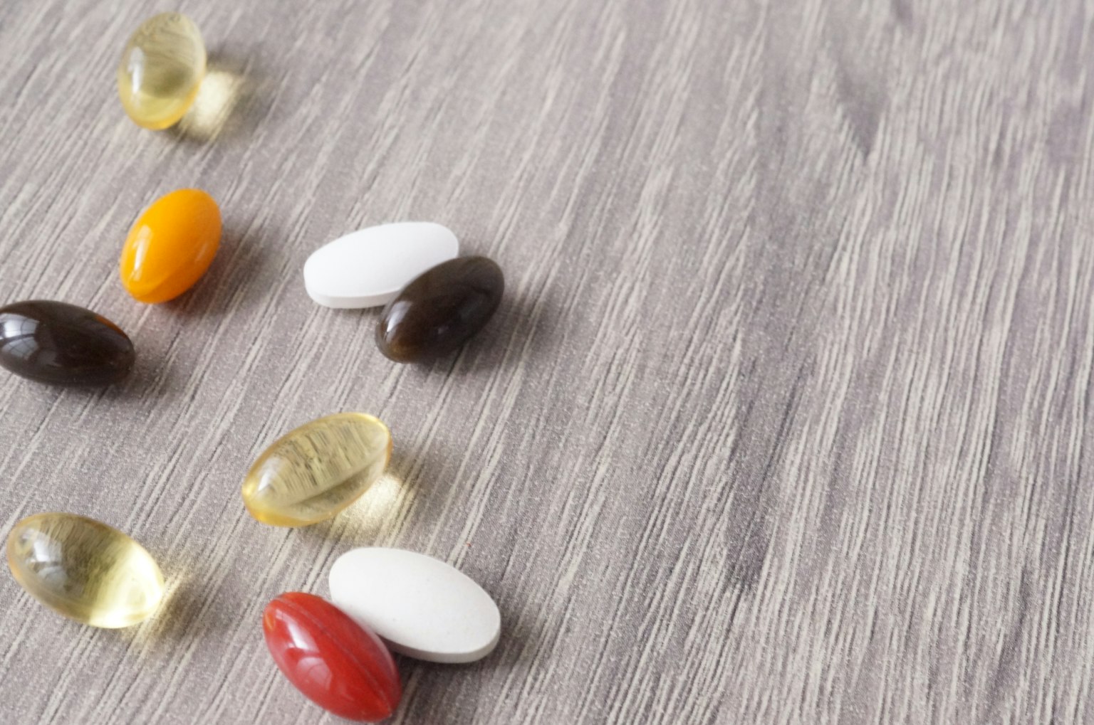 Capsule di integratori colorate sparse su una superficie in legno