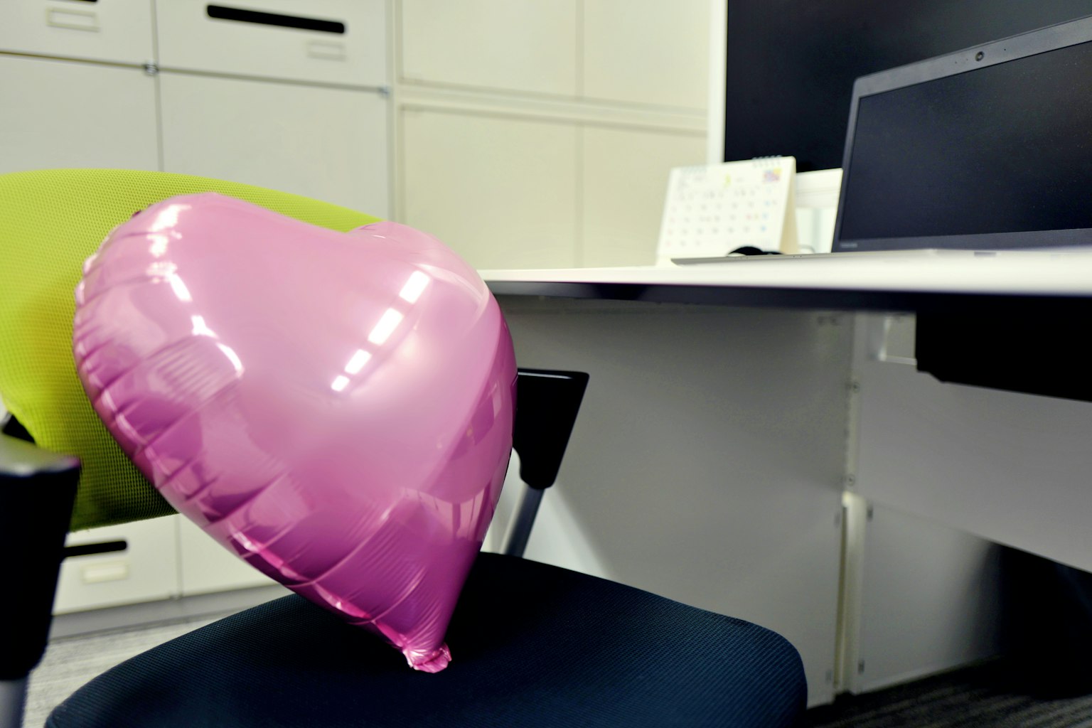 Un palloncino a forma di cuore rosa appoggiato su una sedia in un ufficio