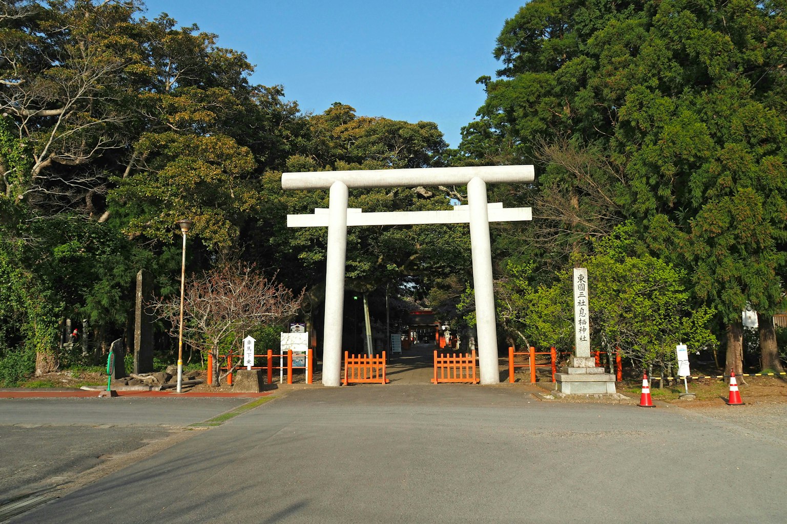 Eingang eines Schreins mit einem weißen Torii, umgeben von üppigen grünen Bäumen