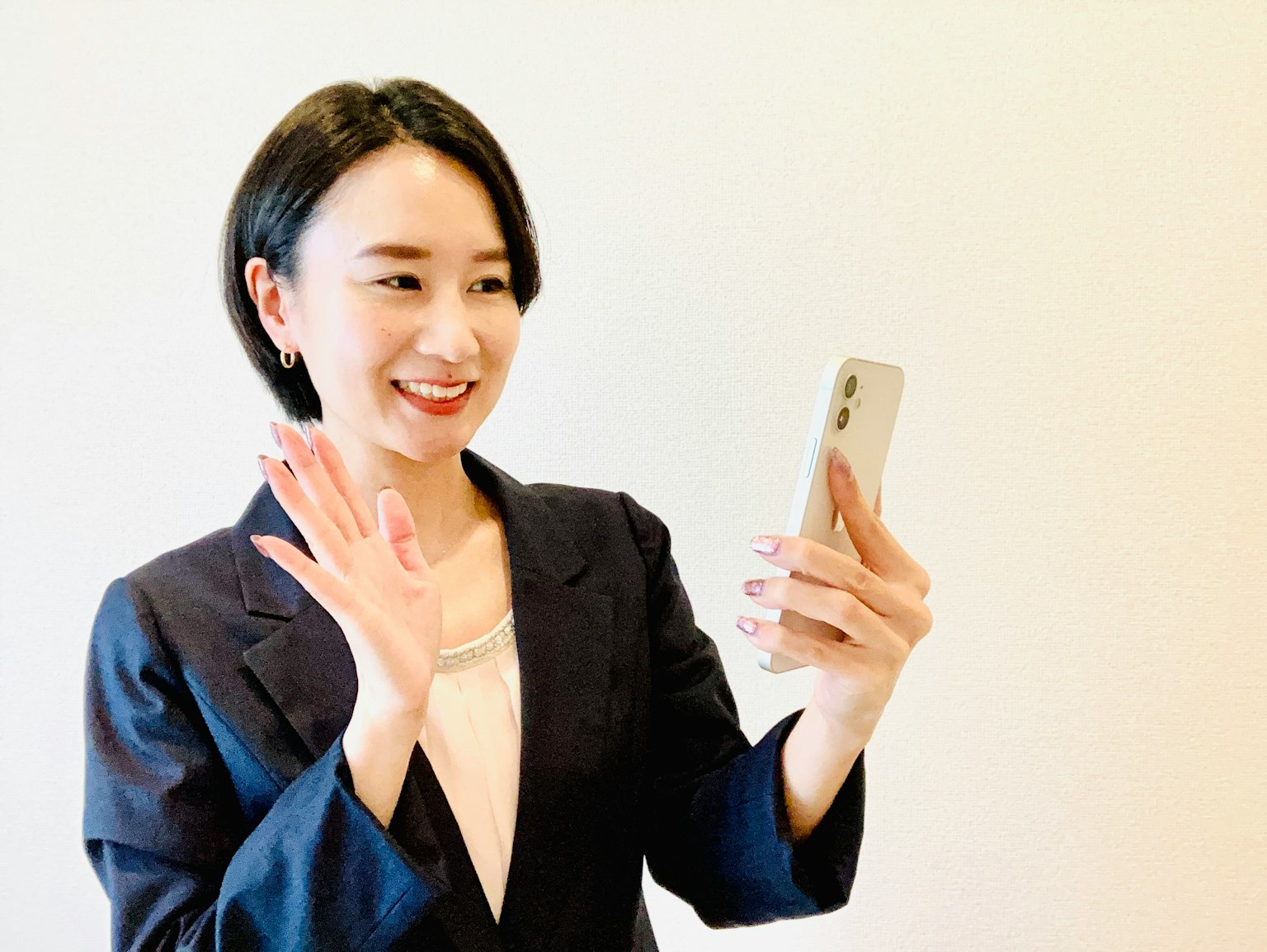Người phụ nữ trong bộ vest cười và vẫy tay trong khi cầm điện thoại thông minh