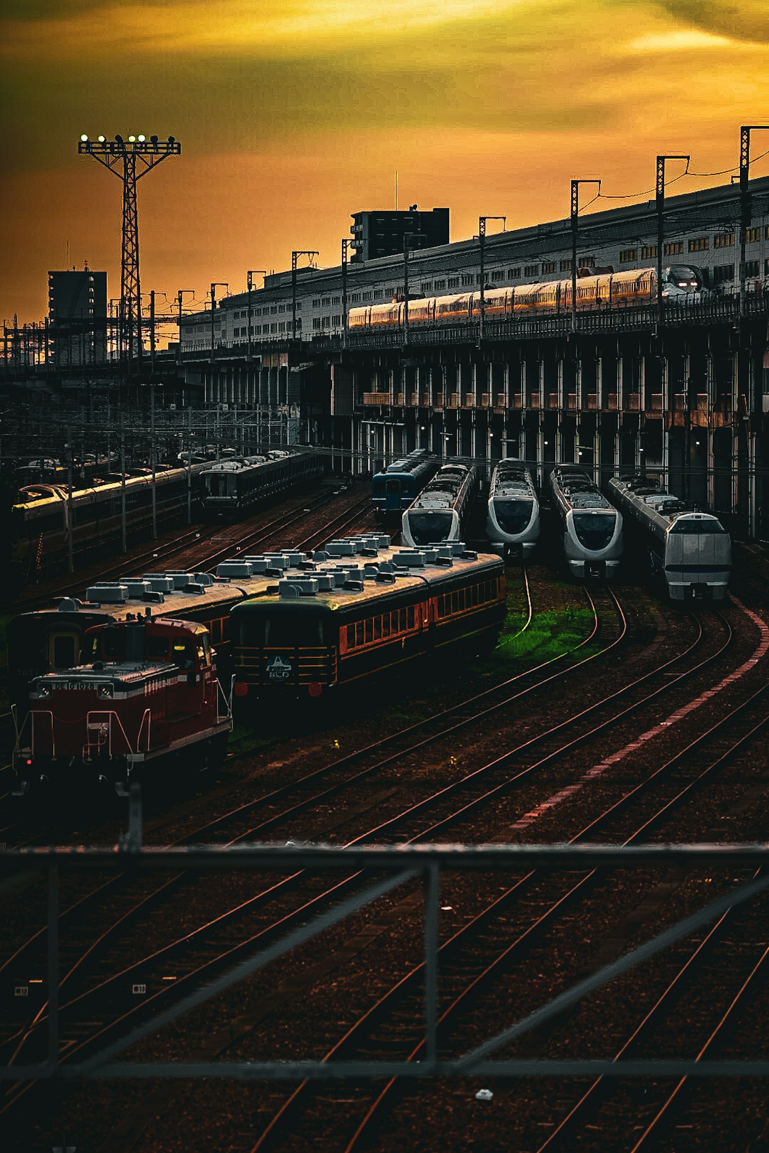 Tempat kereta api saat matahari terbenam dengan beberapa kereta dan rel