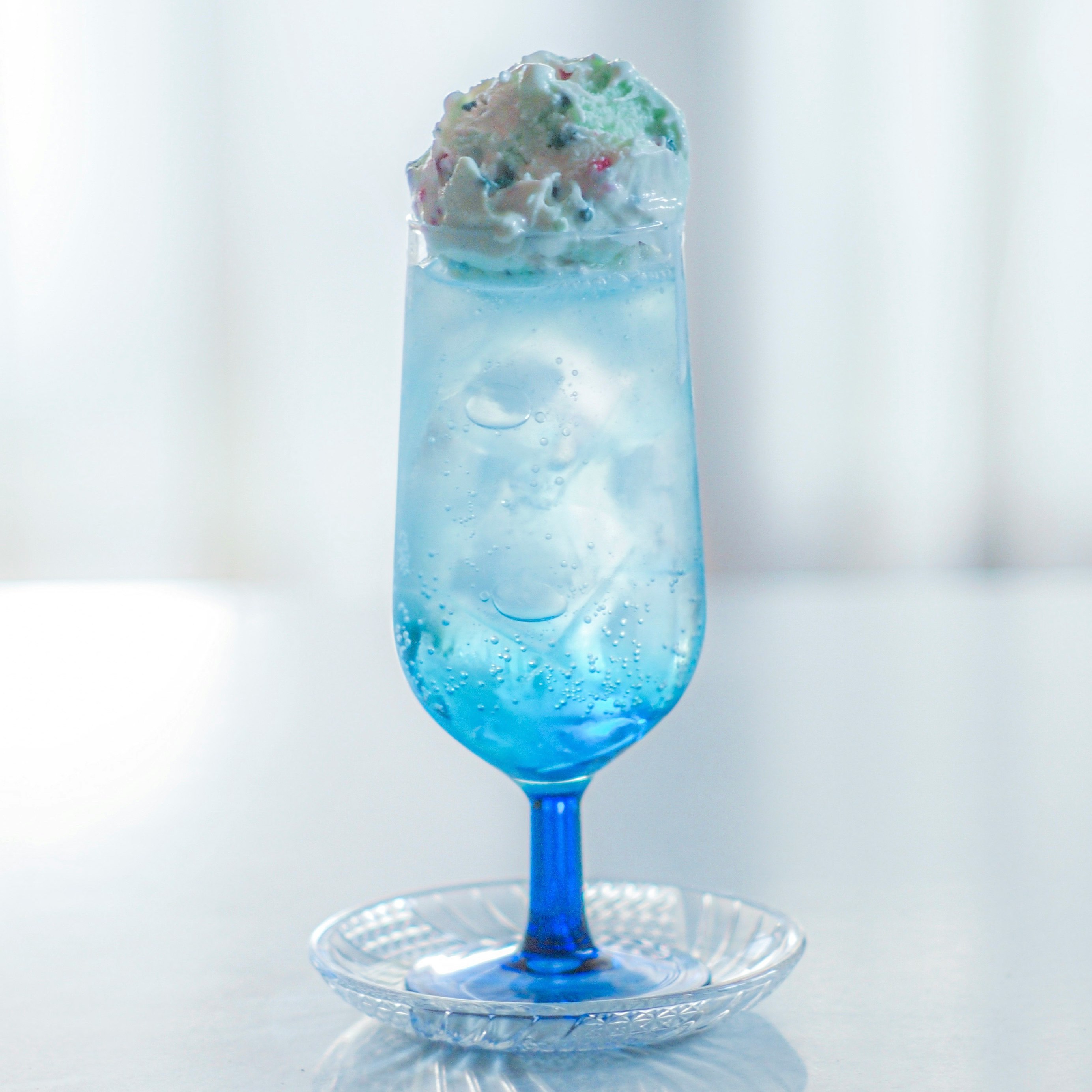 青い炭酸ドリンクのグラスに泡と氷
