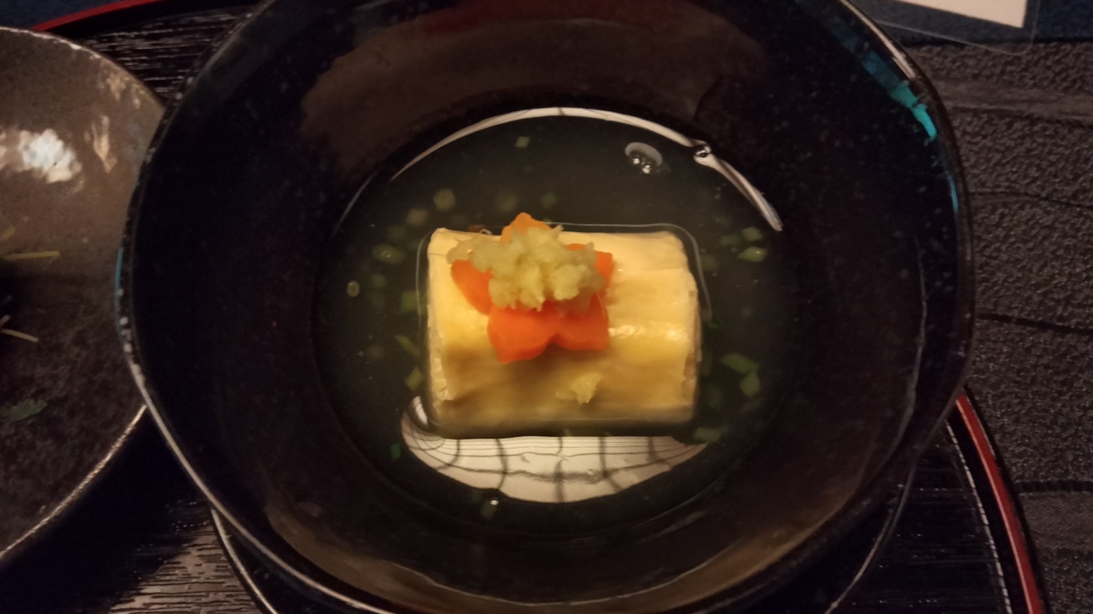 Japanese omelette topped with orange fish roe and green garnish in a black bowl