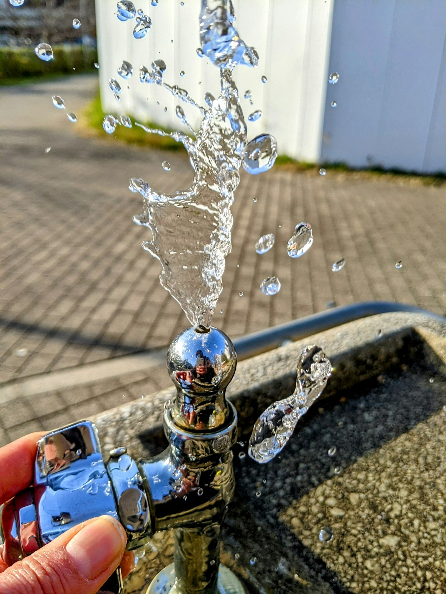 Primo piano di un rubinetto con acqua che sprizza Mano che tiene vicino al getto sotto la luce solare brillante