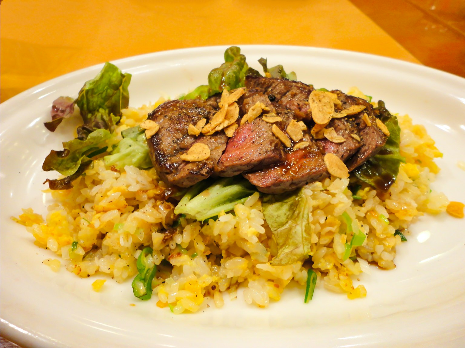 Un plato con carne de res a la parrilla sobre arroz sazonado con verduras y ajo crujiente