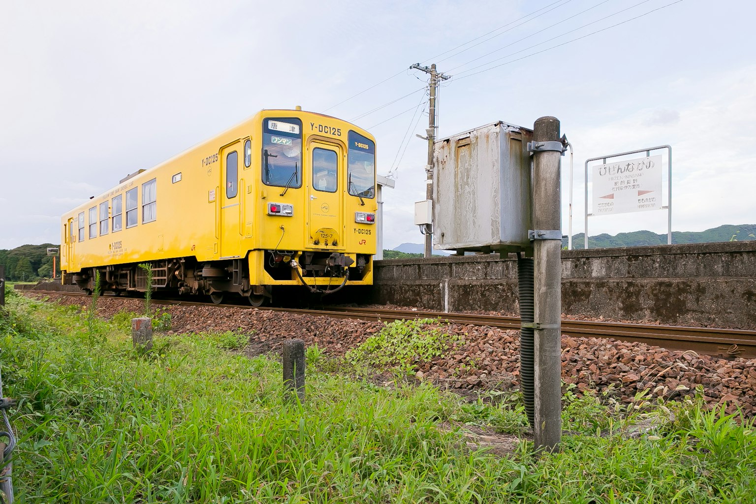 Un train jaune sur les rails avec de l'herbe verte et un poteau de signalisation