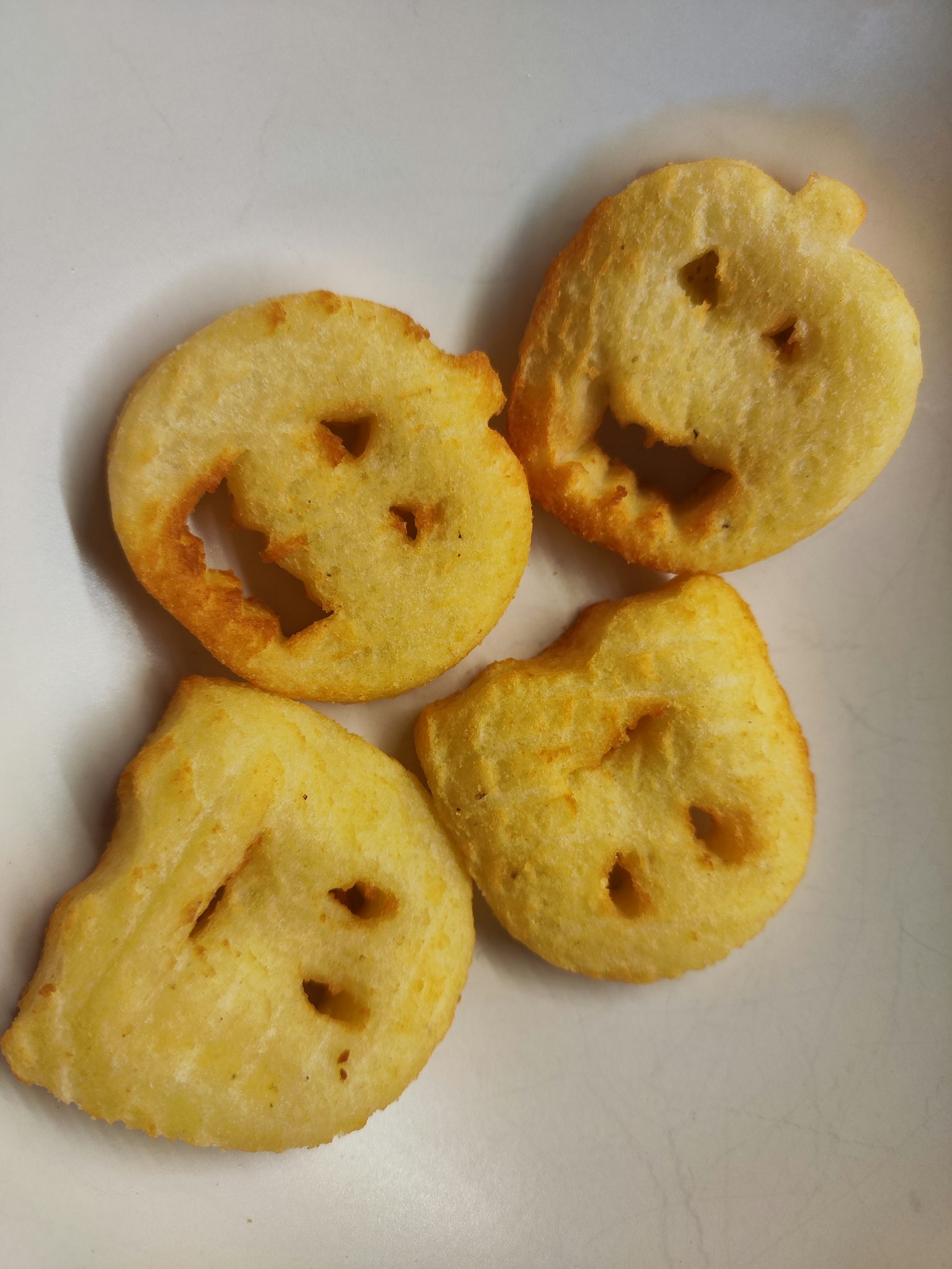 Vier einzigartig geformte frittierte Snacks mit Gesichtern auf einem weißen Teller angeordnet