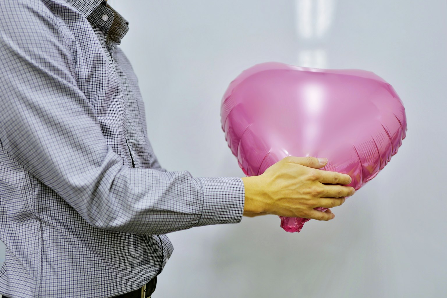 Seorang pria memegang balon berbentuk hati berwarna pink
