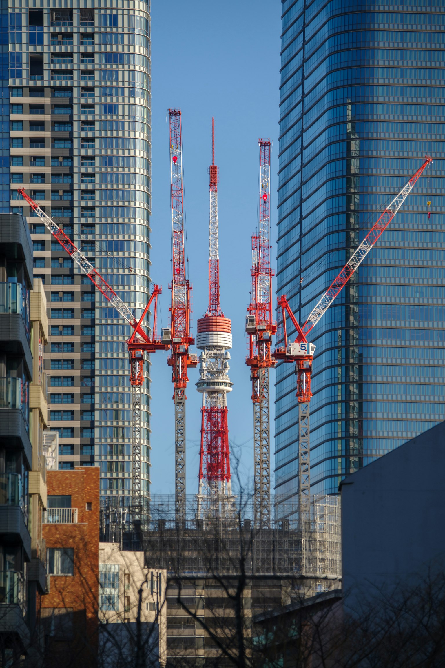 Sitio de construcción con grúas rojas y blancas entre edificios altos en Tokio