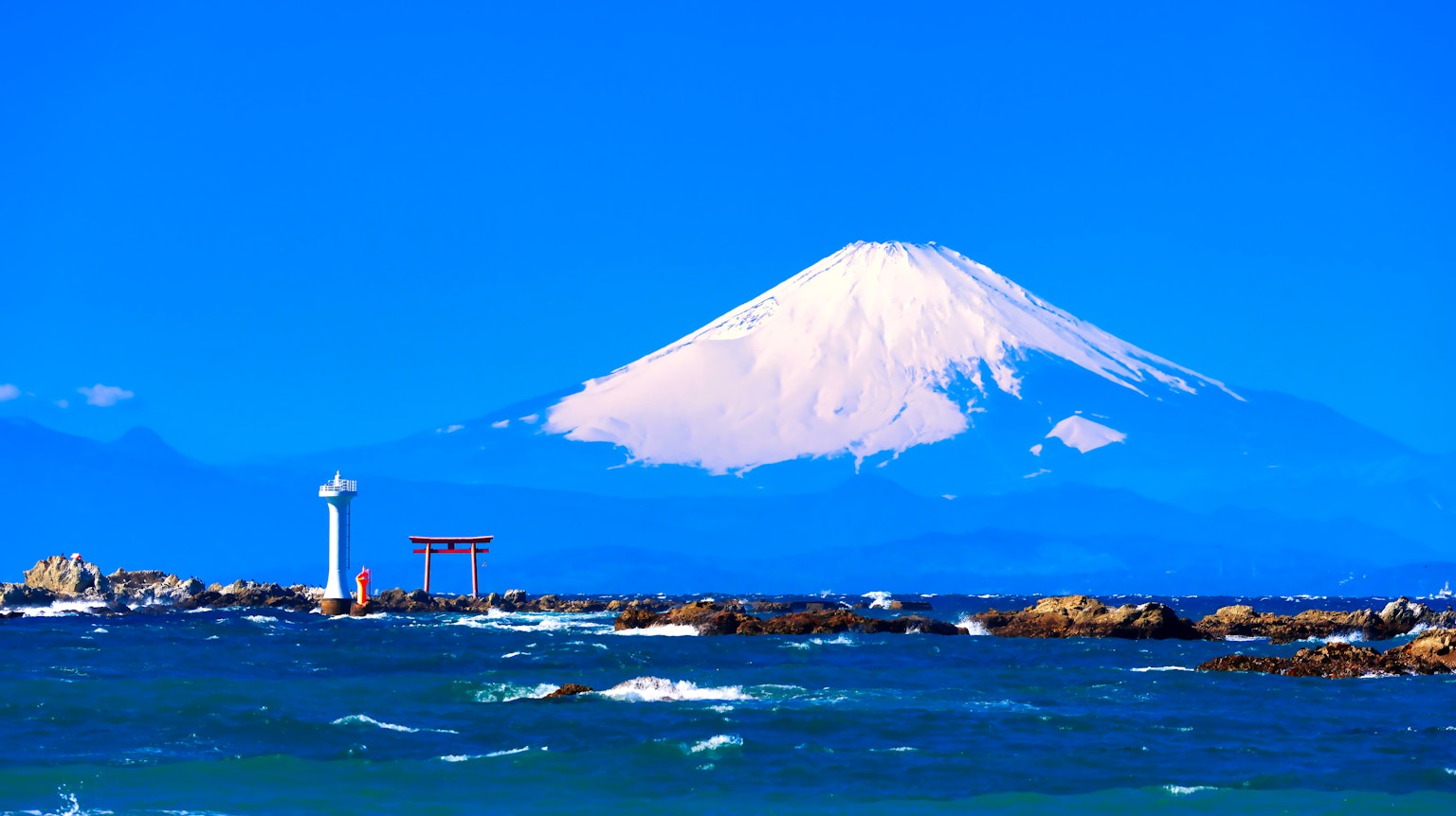 Scenic view of Mount Fuji against a bright blue sky with a lighthouse