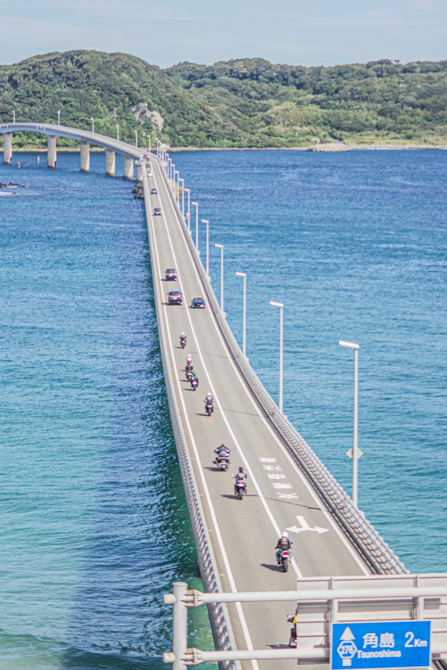 青い海に架かる長い橋を走るバイクの列