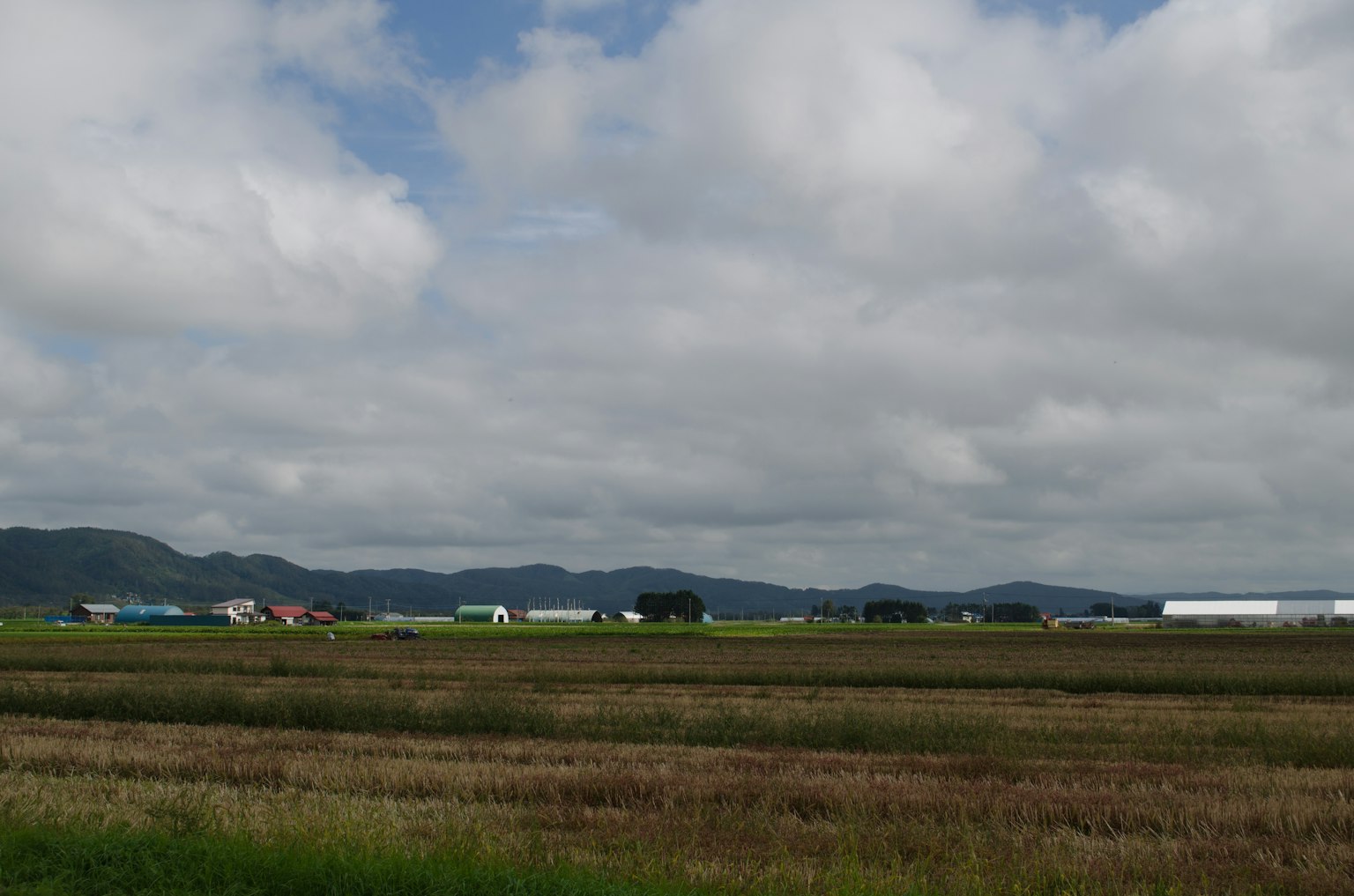 Lanskap pedesaan yang luas dengan ladang dan langit berawan