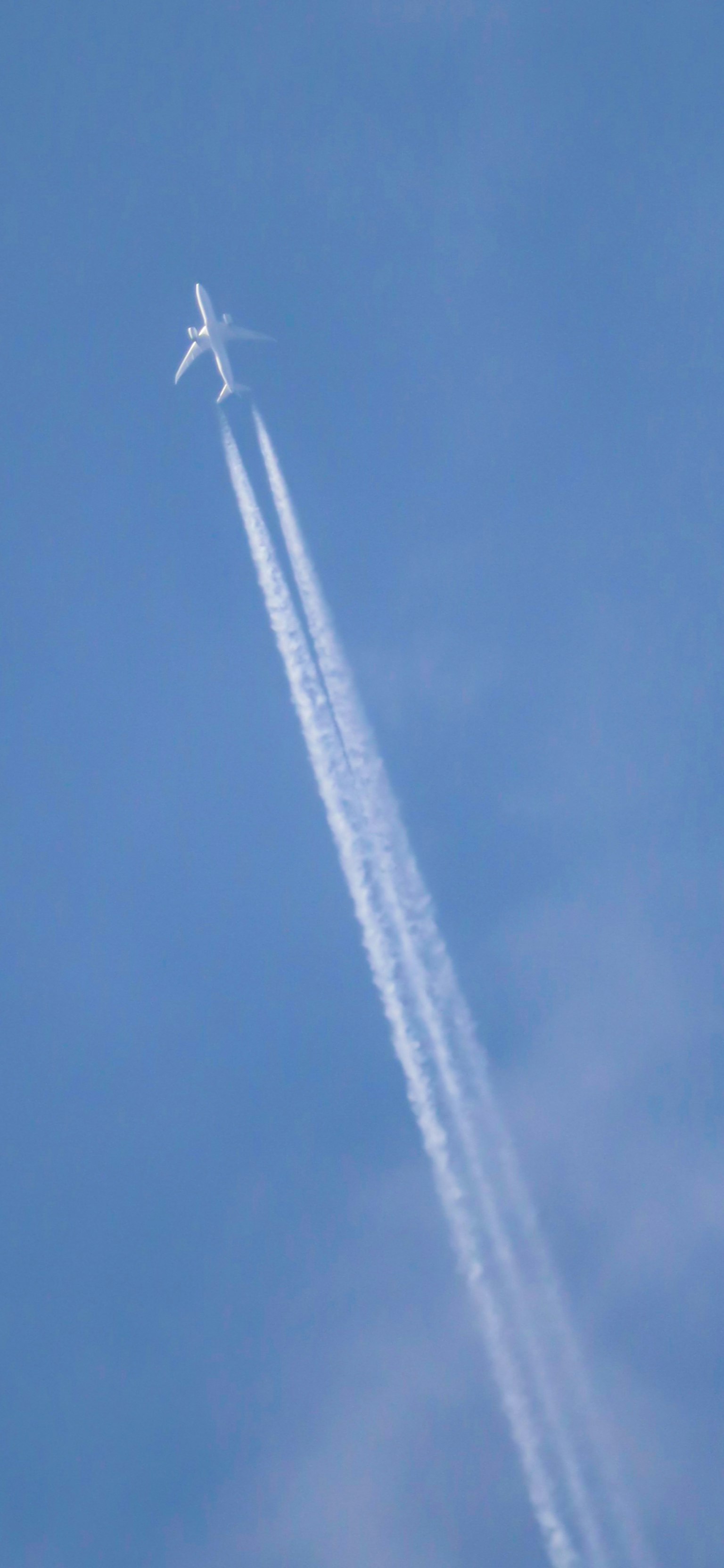 Un avion volant dans un ciel bleu clair laissant une traînée de condensation blanche